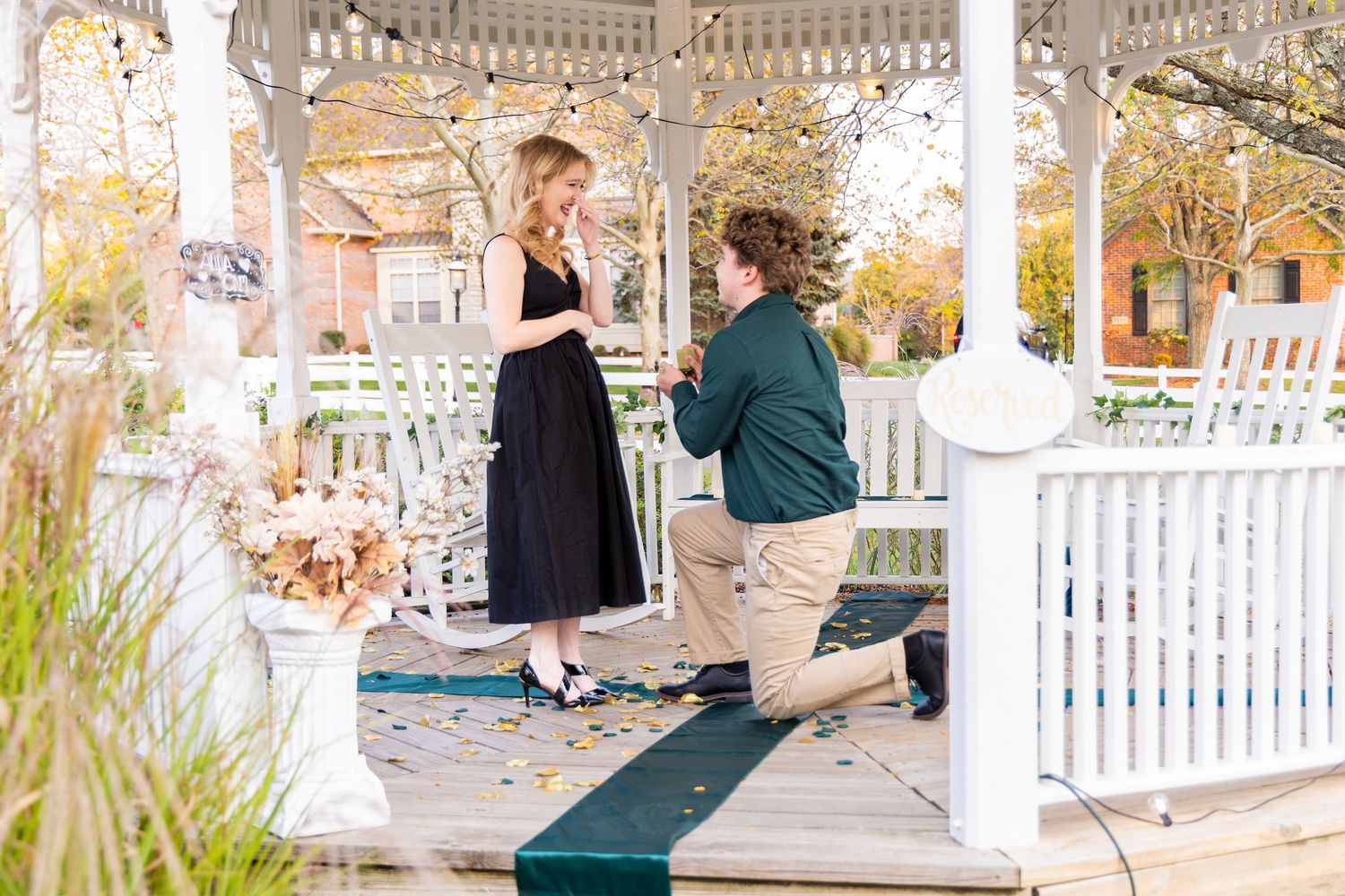 A couple embraces on a white gazebo walkway surrounded by autumn foliage in a romantic setting.