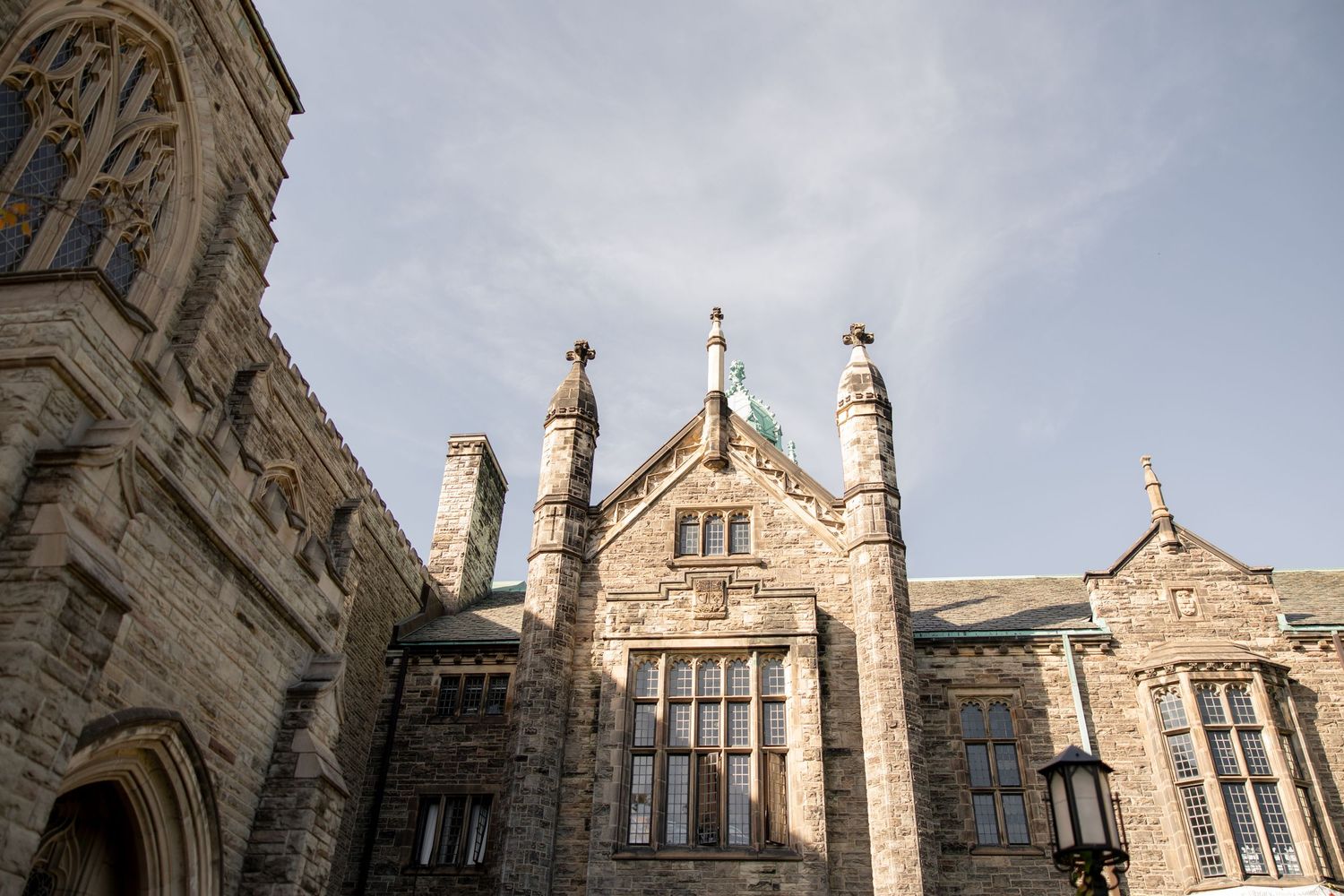 Architectural detail of gothic university building spires against cloudy sky.