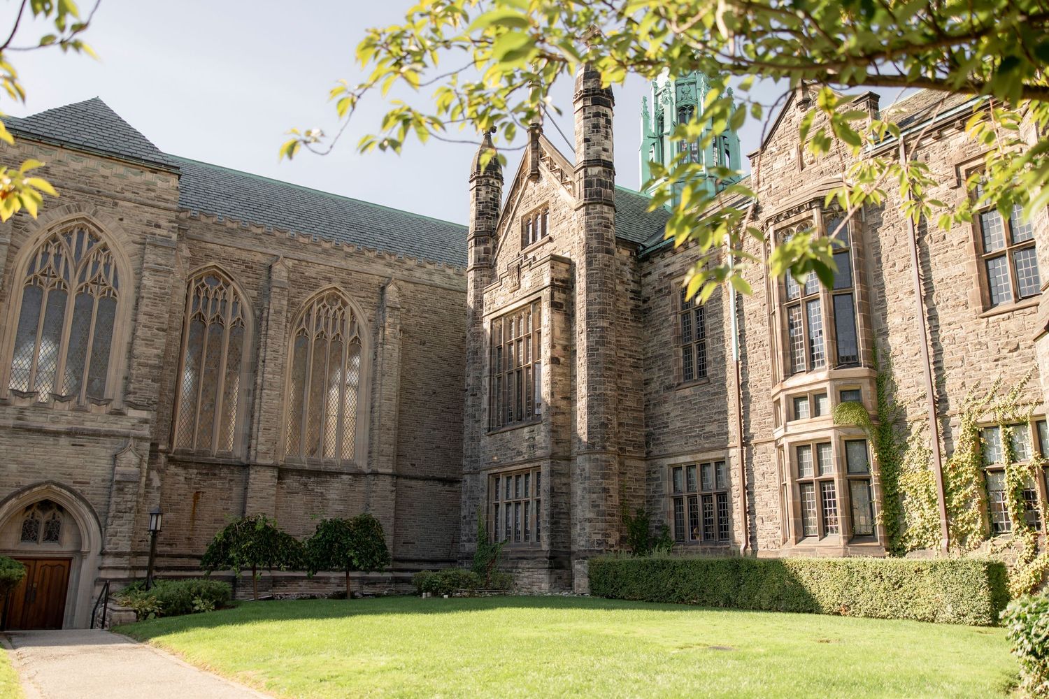 Sunlit exterior of gothic university chapel with manicured lawn.