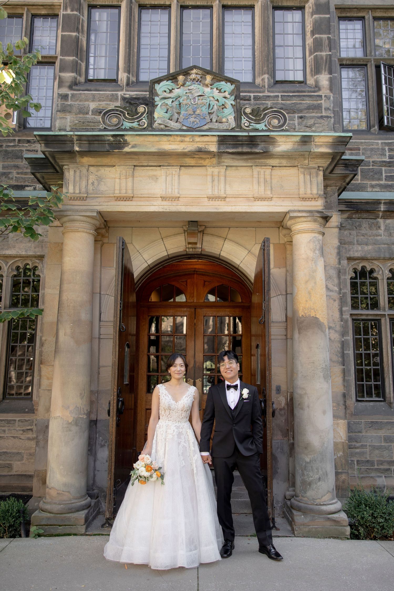 A formal wedding portrait under an ornate stone archway entrance of a historic building.