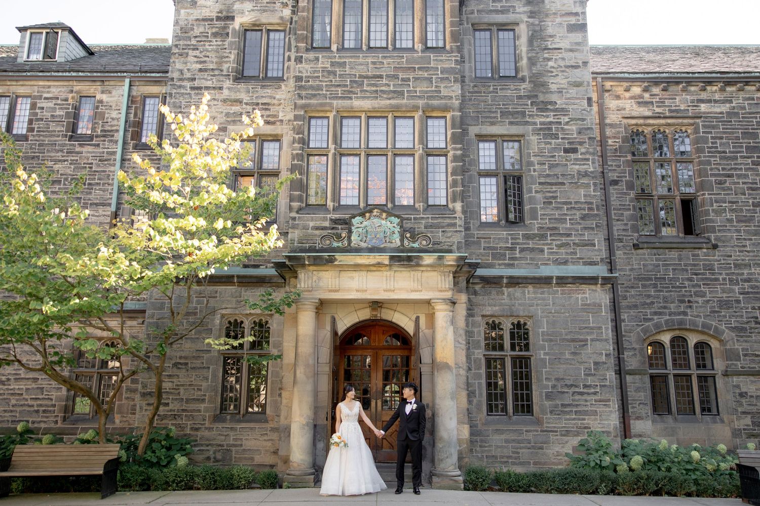 A wedding photo in front of a grand stone building entrance with gothic architecture.