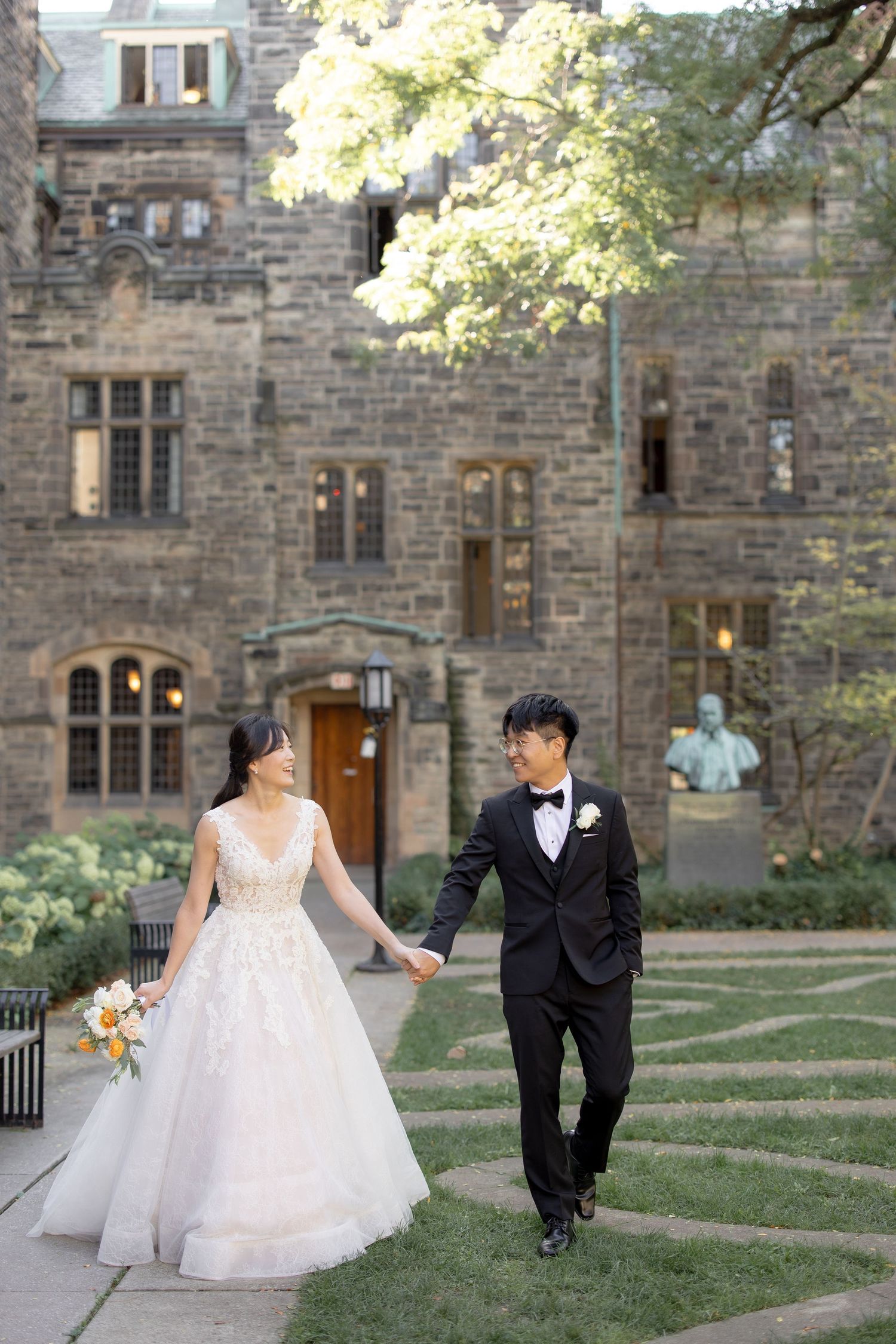 A couple shares a romantic moment in front of a gothic stone castle building with lush greenery.