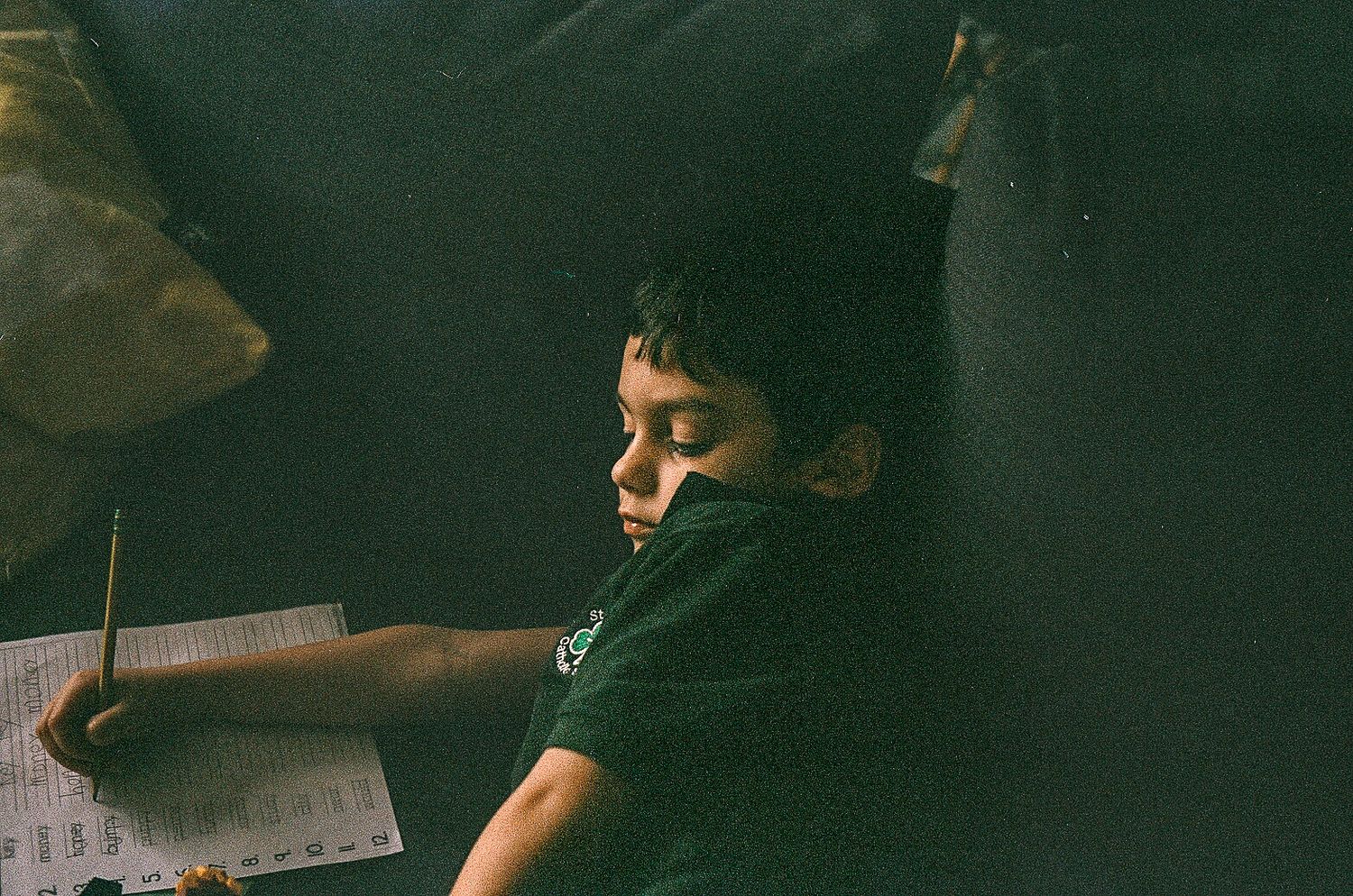 Student writing in notebook in dark classroom setting.