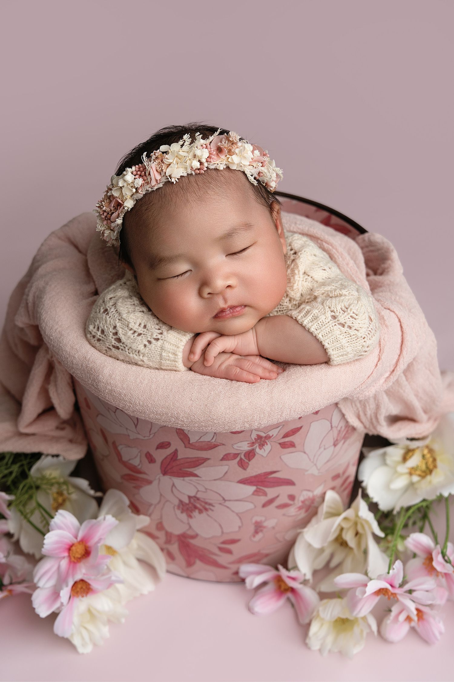 Sleeping baby in floral basket wearing lace outfit and flower crown.