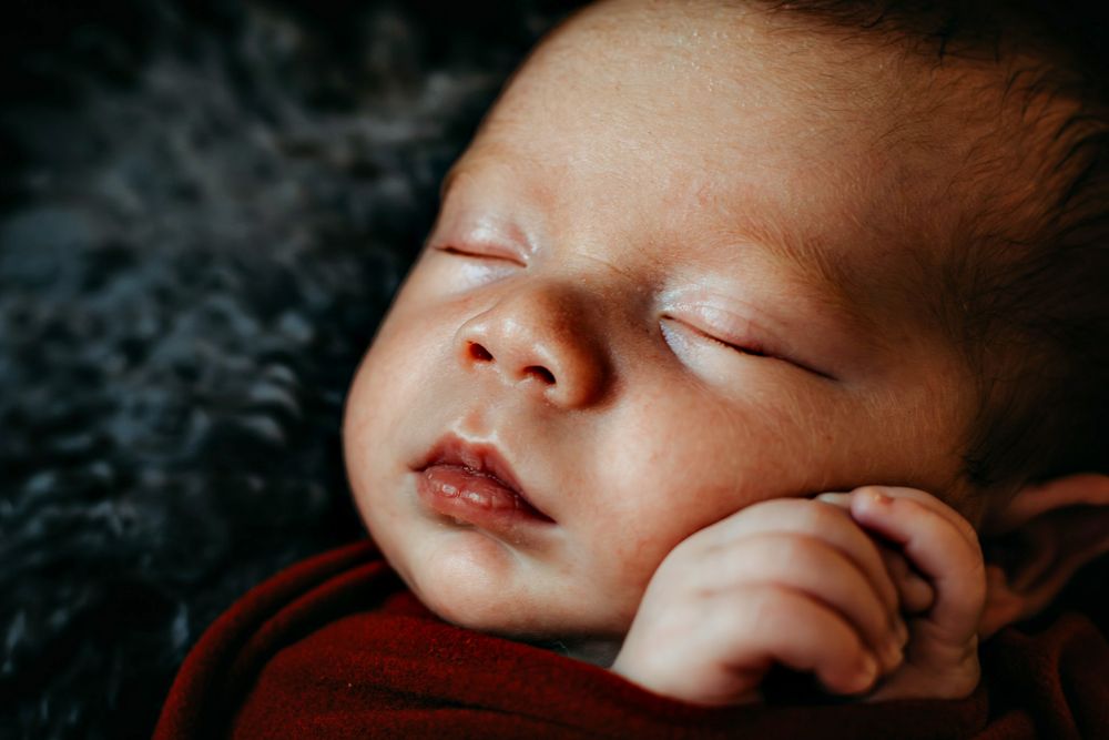 Peaceful sleeping newborn in red wrap against dark background.