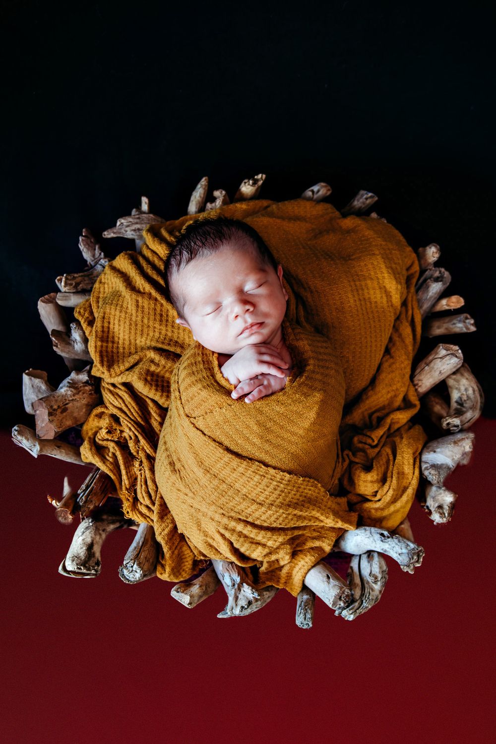 Newborn baby wrapped in mustard yellow blanket surrounded by decorative elements.