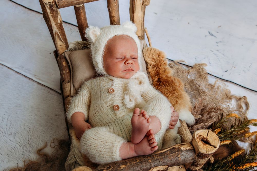 Newborn photography session with soft white blankets and natural wood elements.