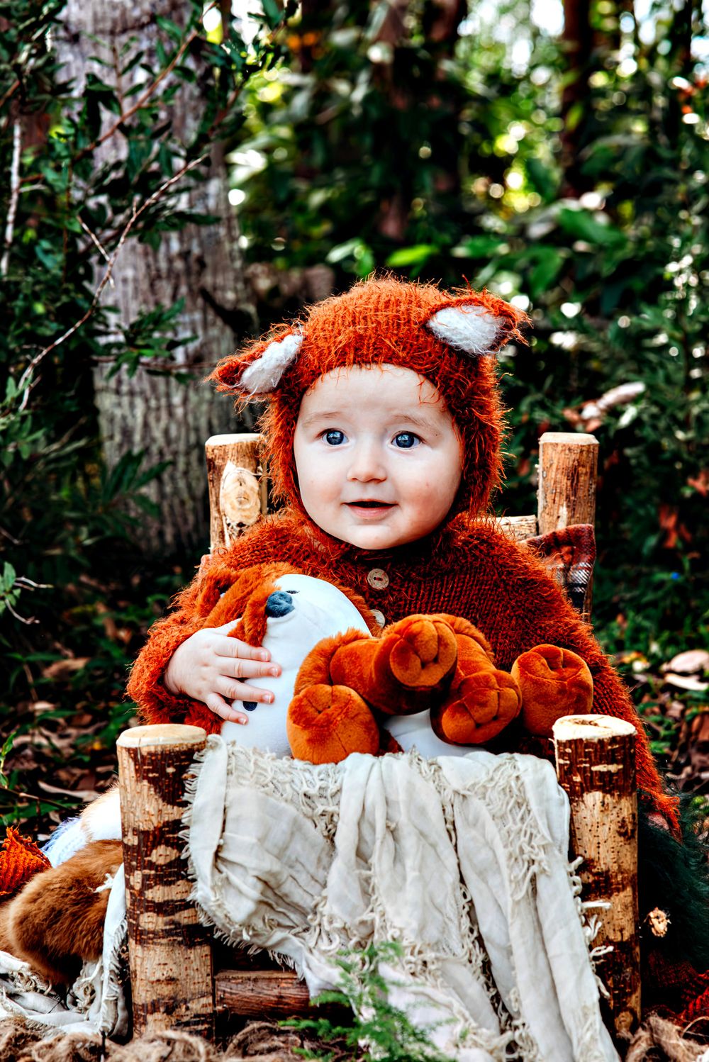 Whimsical woodland themed baby photography with rustic log props and orange fox costume.
