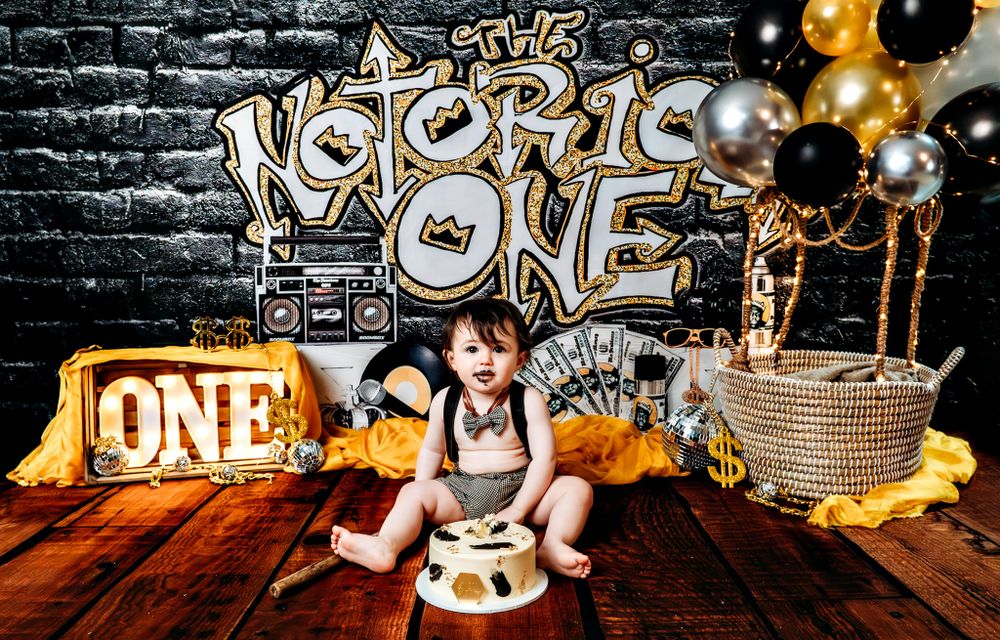 First birthday cake smash photo session with graffiti wall backdrop and gold balloons.