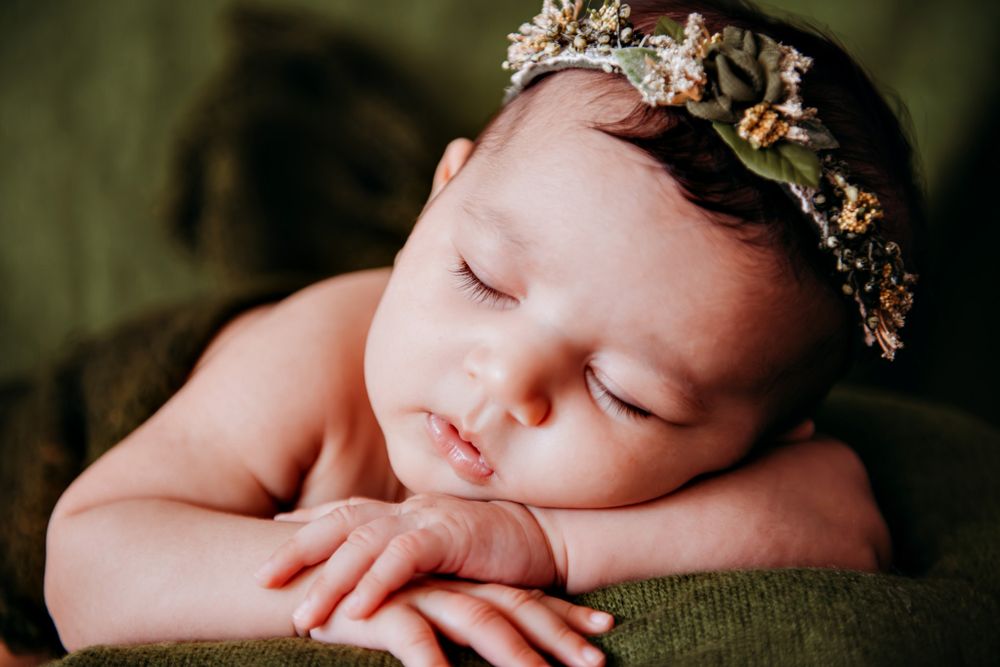 Artistic newborn photography with delicate floral crown and dark moody backdrop.