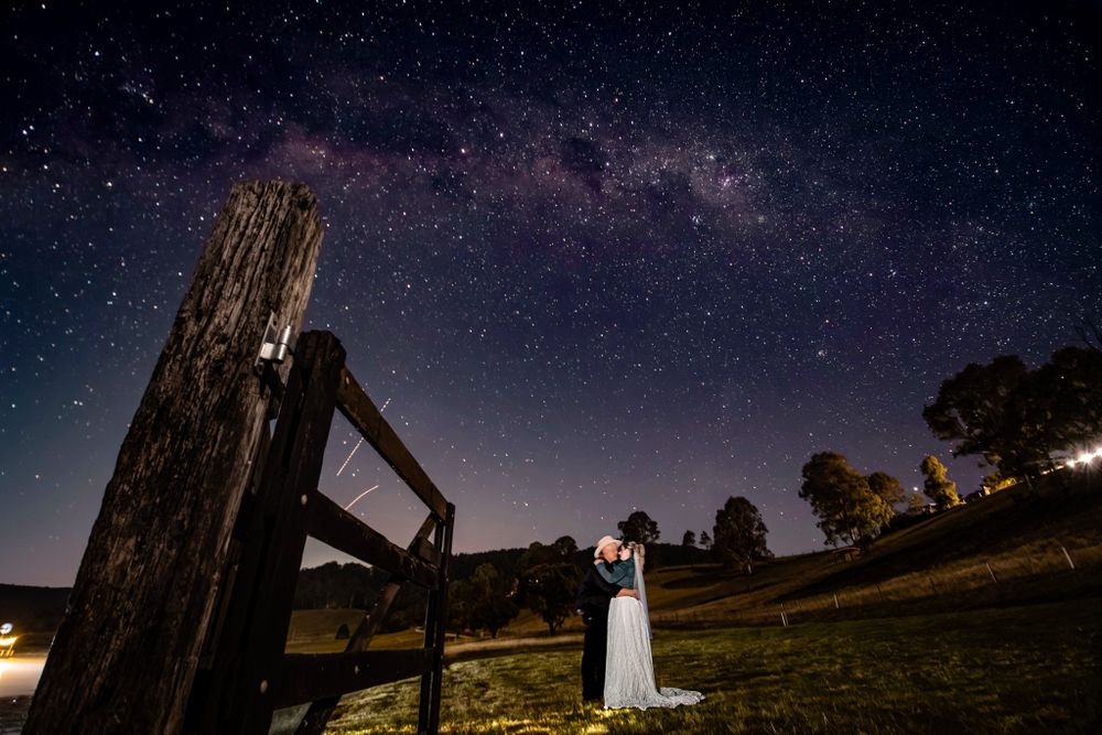 Wedding photography session under a starry night sky with silhouettes against dramatic lighting.
