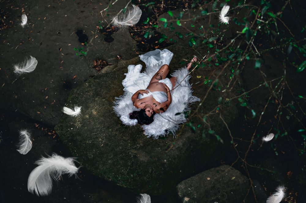 Artistic overhead photo of person lying in snow surrounded by white feathers at night.