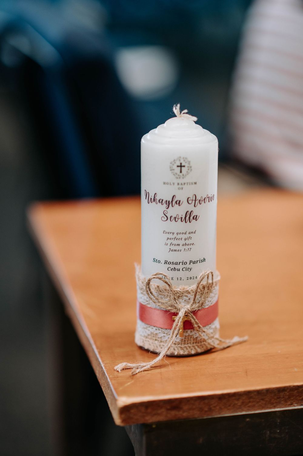 Decorative white baptism candle with lace and ribbon accents on wooden surface.