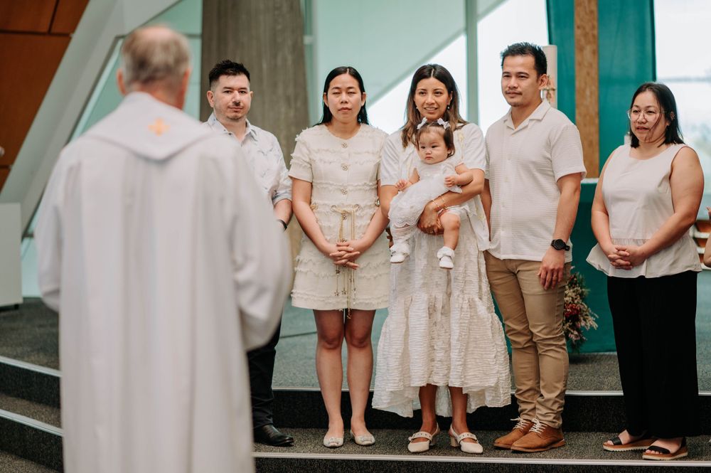 Family gathering with clergy member at church entrance wearing white clothing.