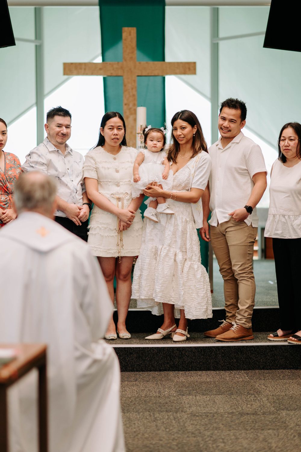 Family gathered near wooden cross during religious ceremony wearing coordinated outfits.