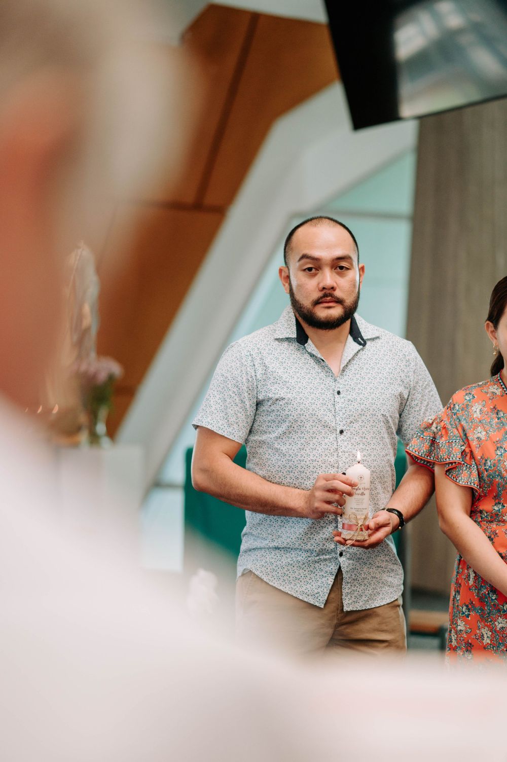 Person in polka dot button-down shirt holding a drink at a social gathering.