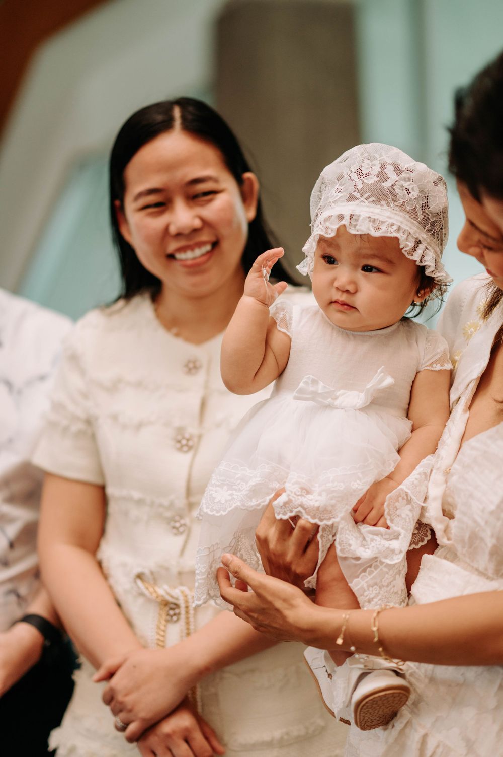 Baby in white christening dress and bonnet being held during baptism ceremony.