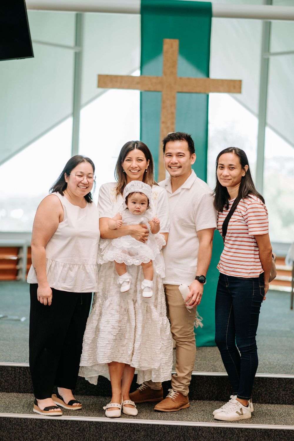 Family group photo in church with wooden cross and teal accent wall in background.