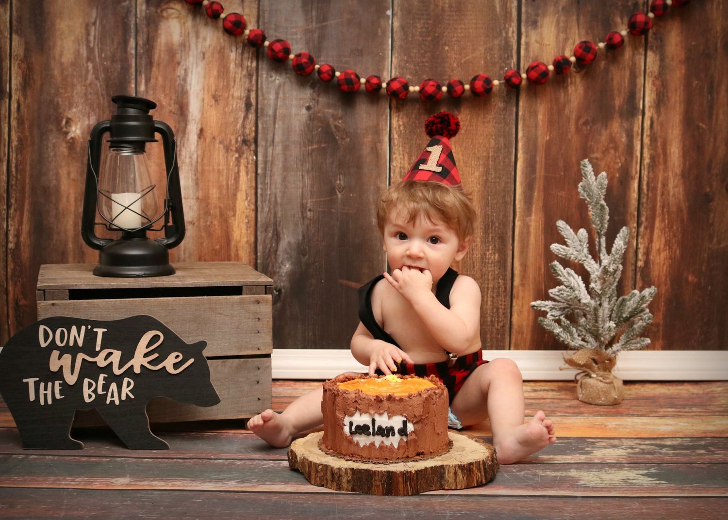 Rustic holiday setup with lantern, wooden crate and small decorated Christmas tree against dark wood wall.