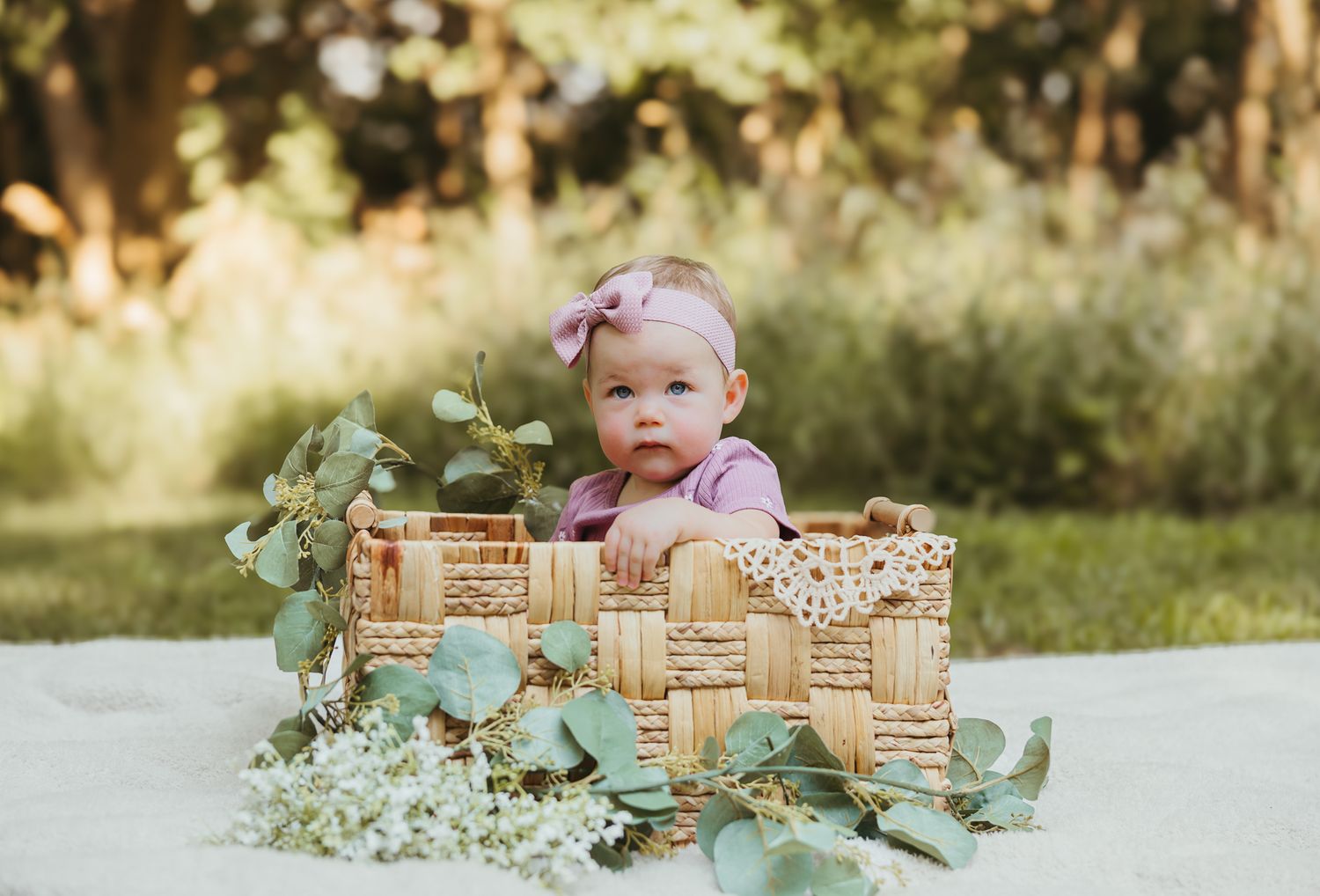 Baby sitting in decorative wicker basket with eucalyptus and baby's breath flowers outdoors. Colorado Springs Photographer.