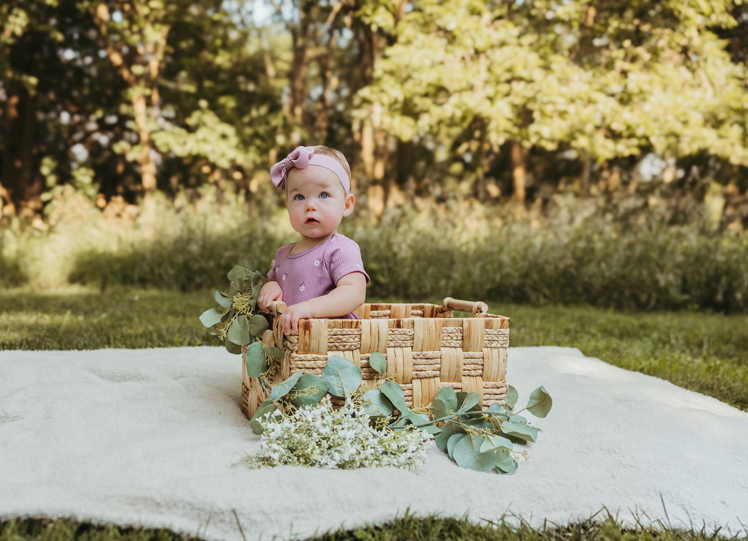 Natural light photography setup with a wicker basket and botanical accents on white fabric. Colorado Springs Photographer.