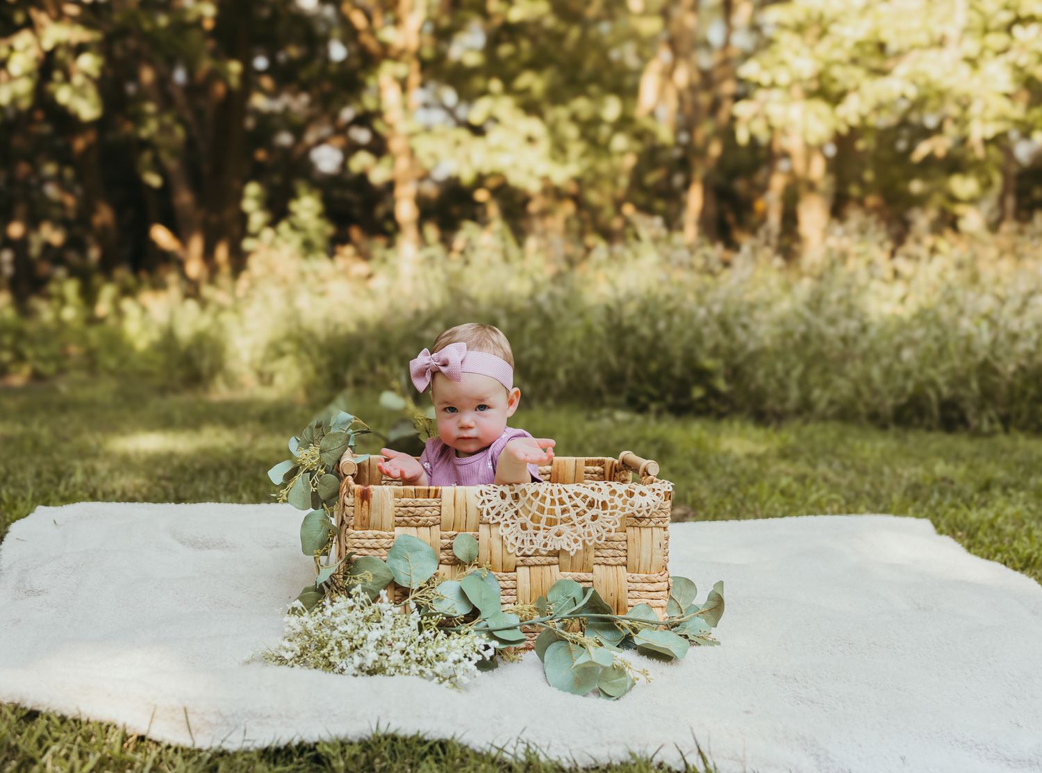 A decorative basket scene with lace and eucalyptus leaves set on white fabric outdoors. Colorado Springs Photographer.