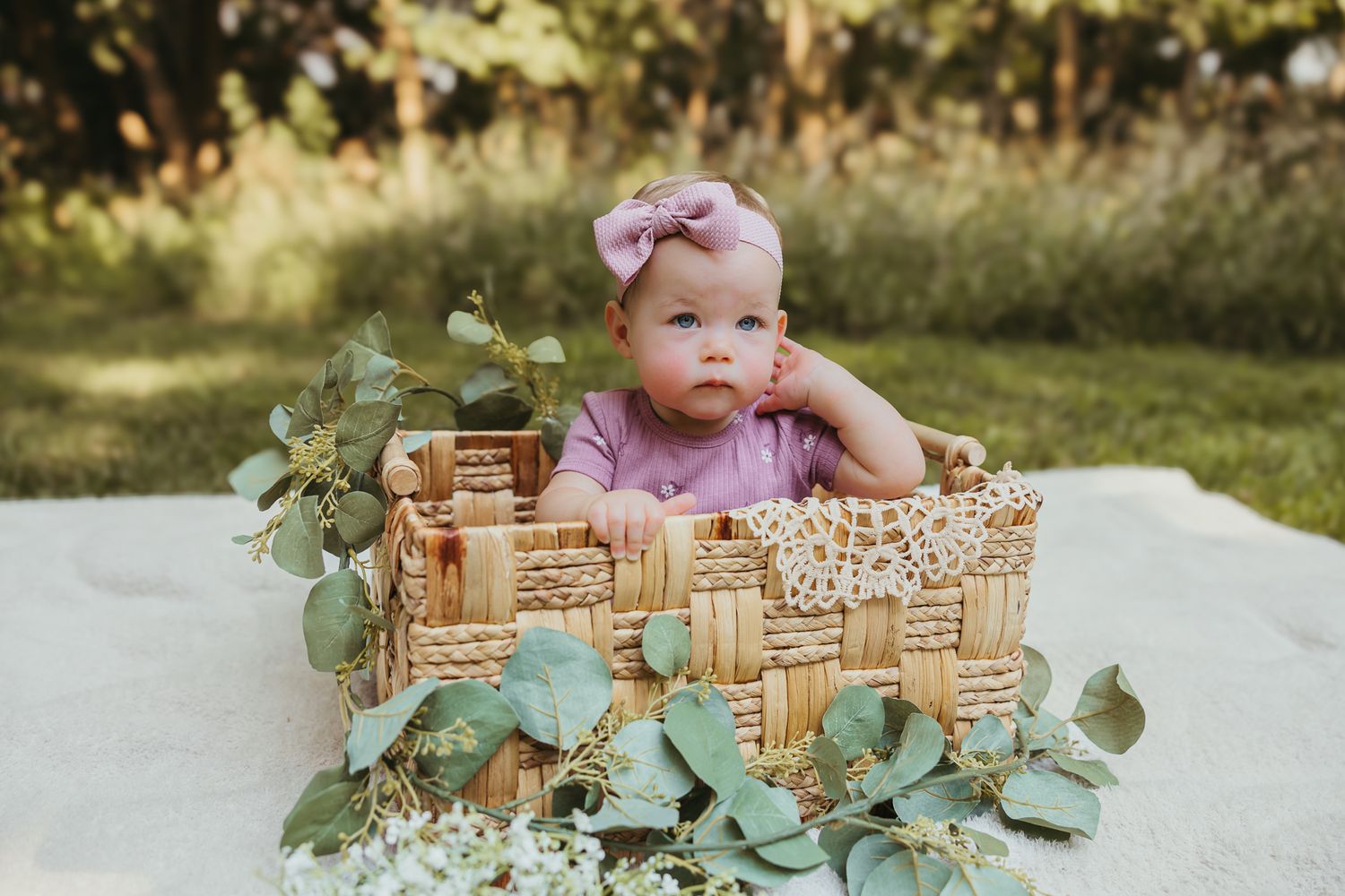 A decorated wicker basket with lace trim and eucalyptus leaves on a white blanket outdoors. Colorado Springs Photographer.