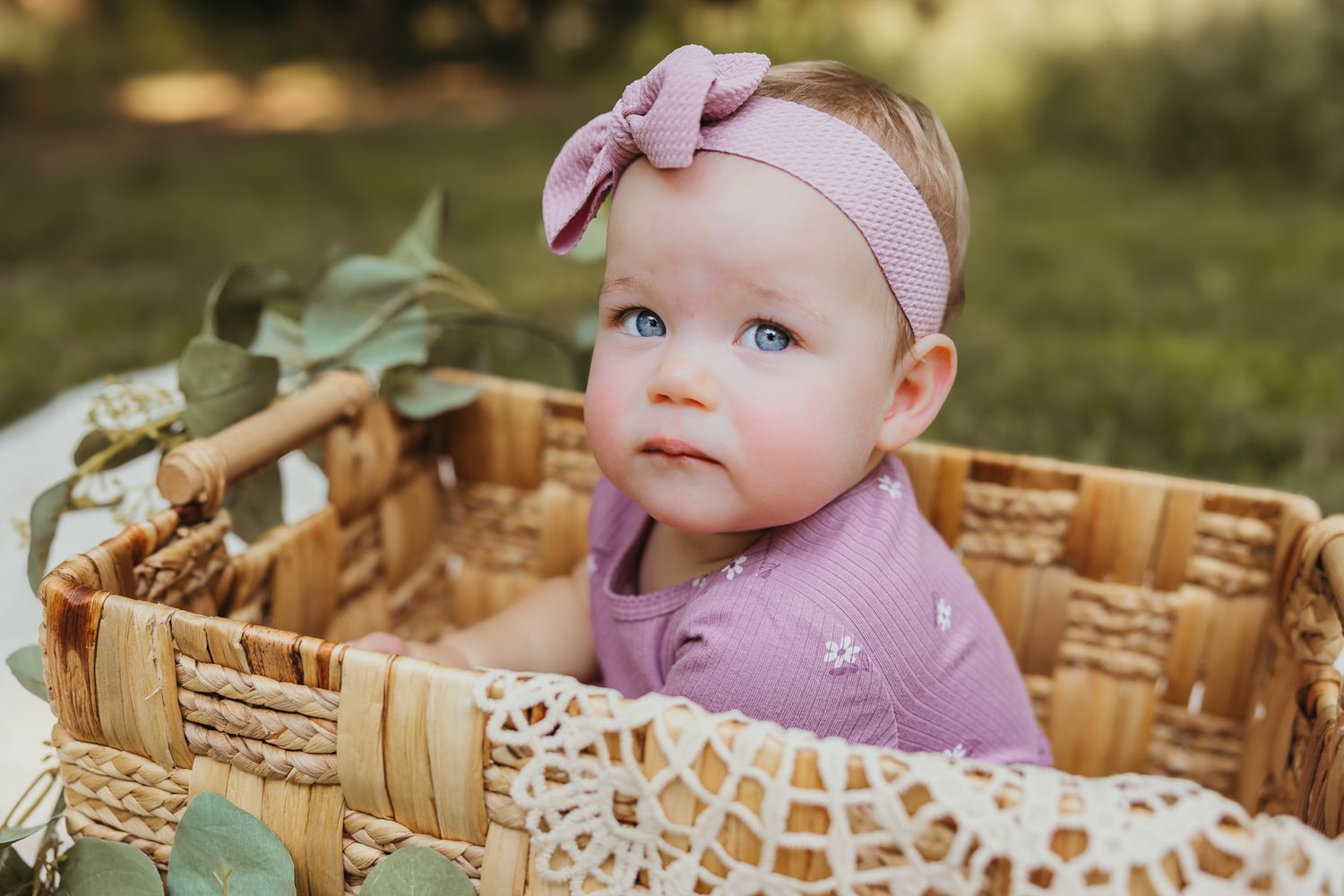 A woven basket decorated with lace and eucalyptus leaves creates a charming outdoor photo setting. Colorado Springs Photographer.