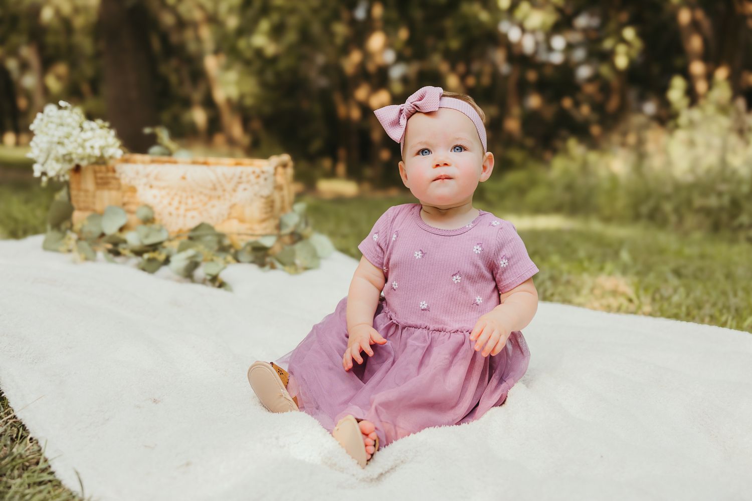 Baby in mauve dress sitting on white blanket during outdoor garden photoshoot. Colorado Springs Photographer.