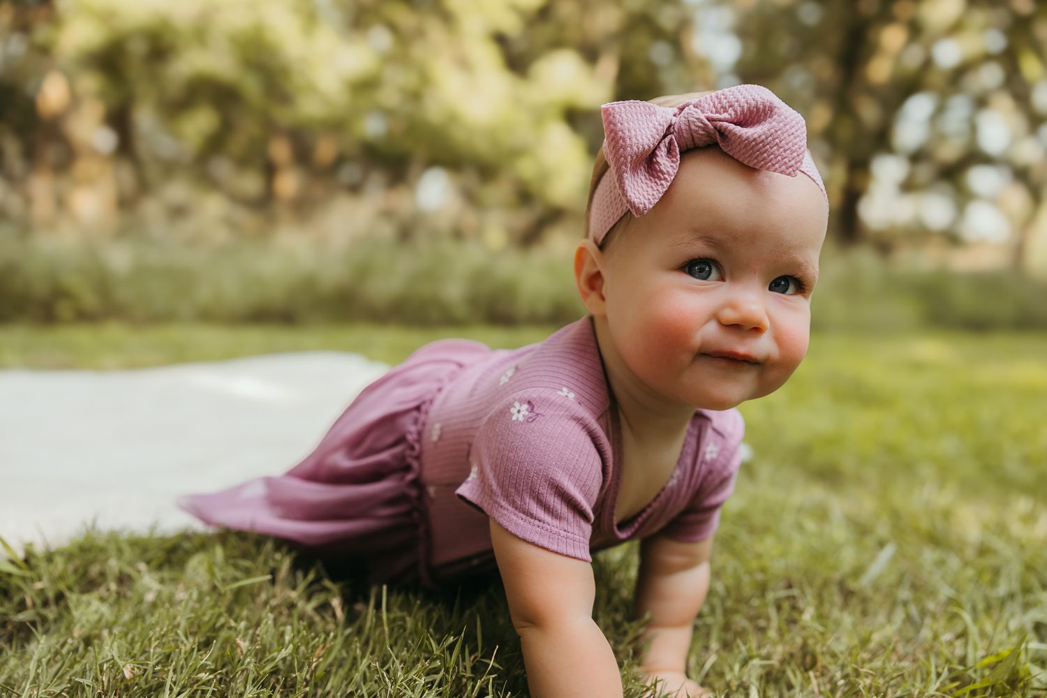 Baby in mauve dress and bow crawling on grass during outdoor photo session. Colorado Springs Photographer.