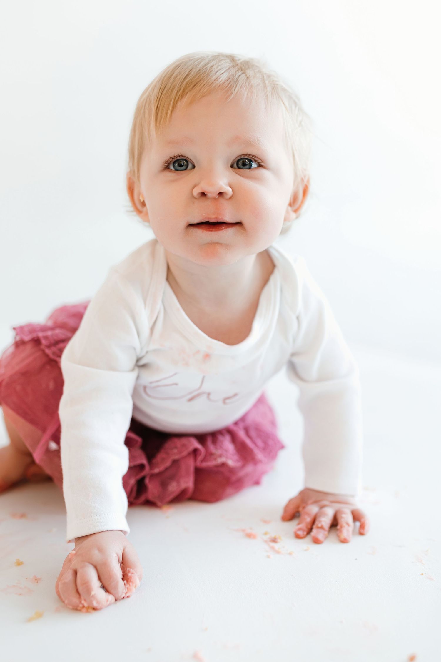 Baby in white long sleeve shirt and pink tutu crawls on white floor with bright smile. Colorado Springs Photographer.