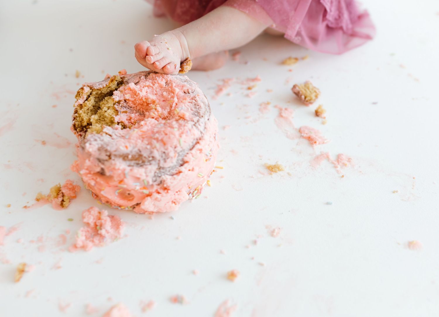 Pink smashed birthday cake crumbs and frosting scattered on a white surface. Colorado Springs Photographer.