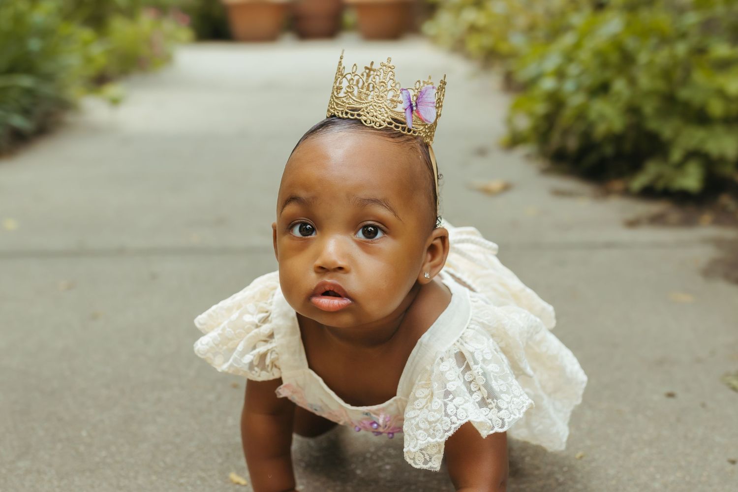 Baby wearing a gold crown and white ruffled dress crawling outdoors. Colorado Springs Photographer.