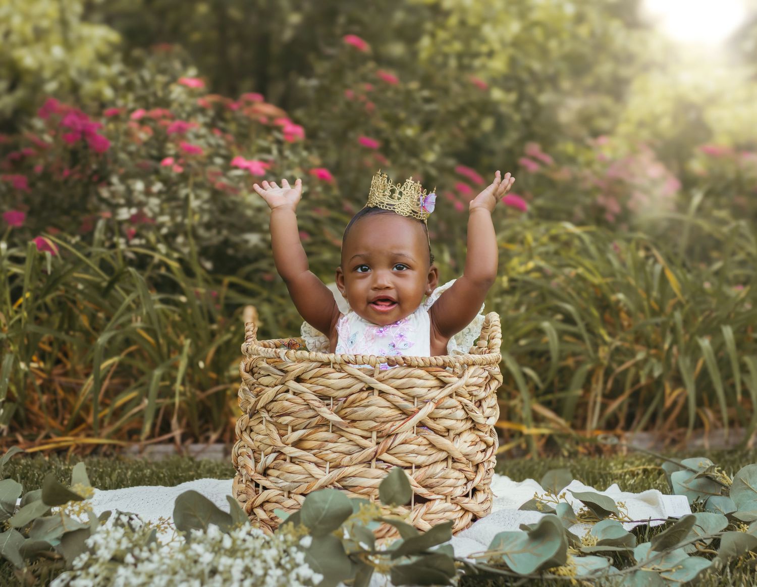 A happy baby raises their arms in celebration while sitting in a woven basket outdoors. Colorado Springs Photographer.