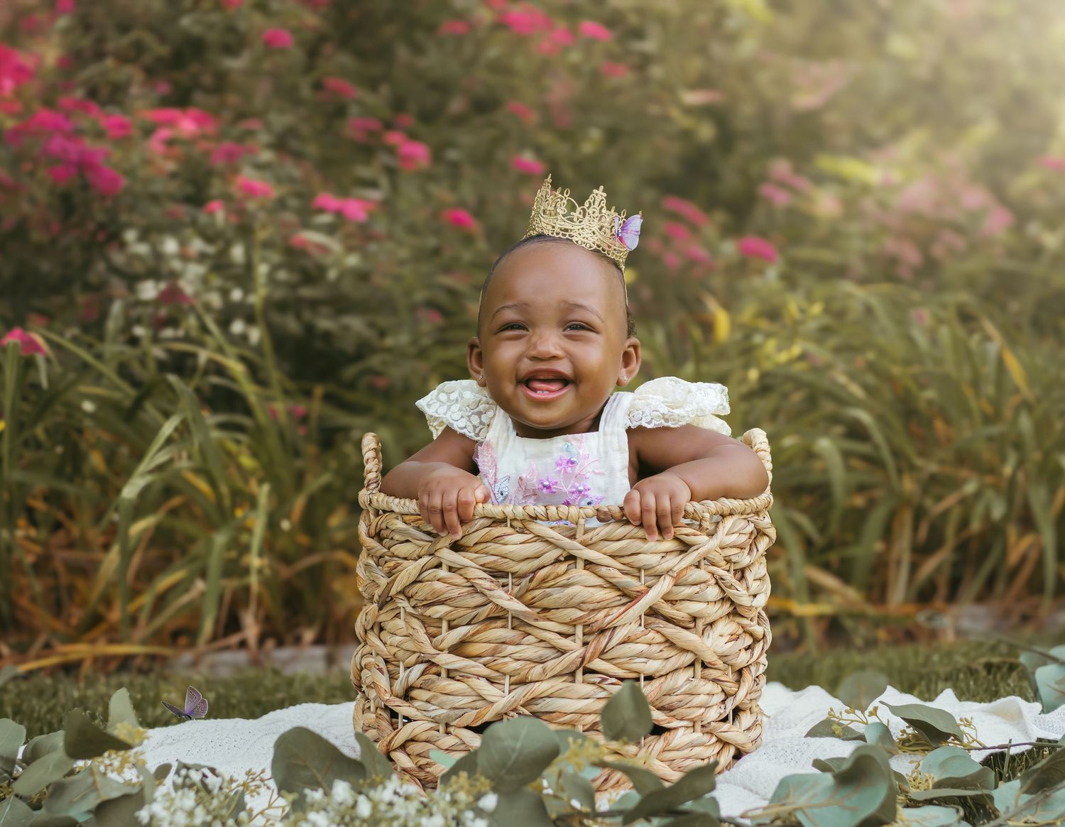 An enthusiastic baby wearing a crown leans on the edge of a woven basket in a garden setting. Colorado Springs Photographer.