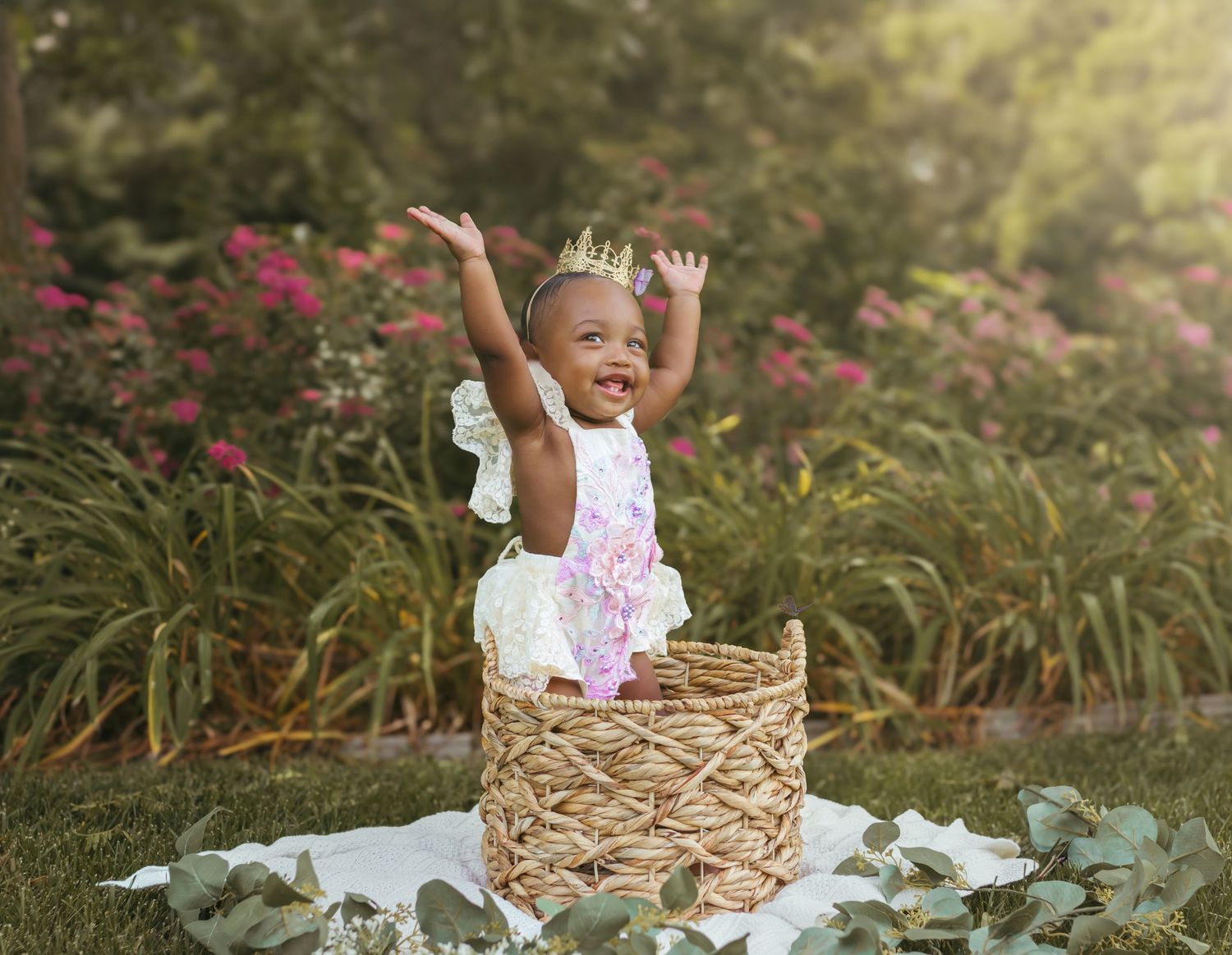An excited baby raises their hands while standing in a decorative basket with a garden background. Colorado Springs Photographer.