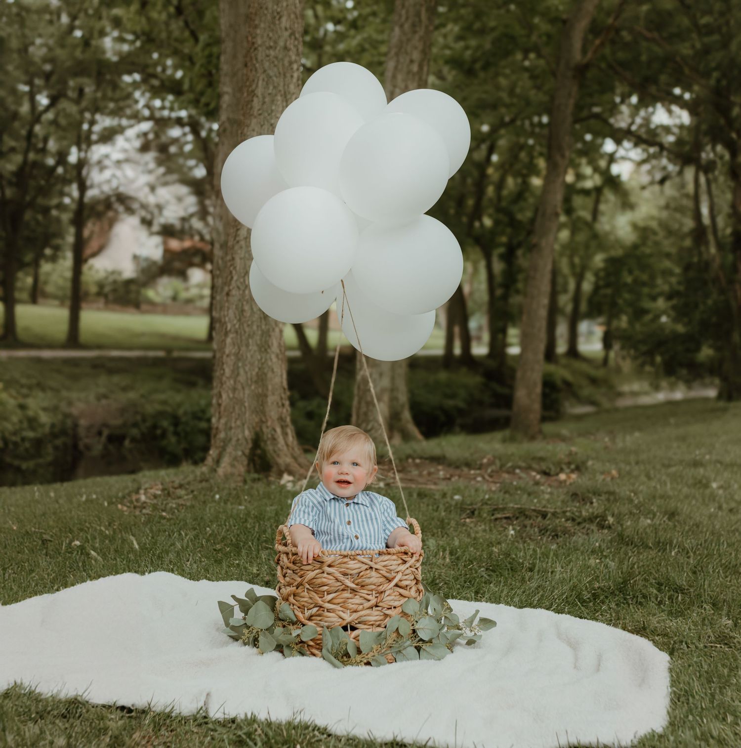 A rustic outdoor photo shoot setup with white balloons and a woven basket on a white blanket. Colorado Springs Photographer.