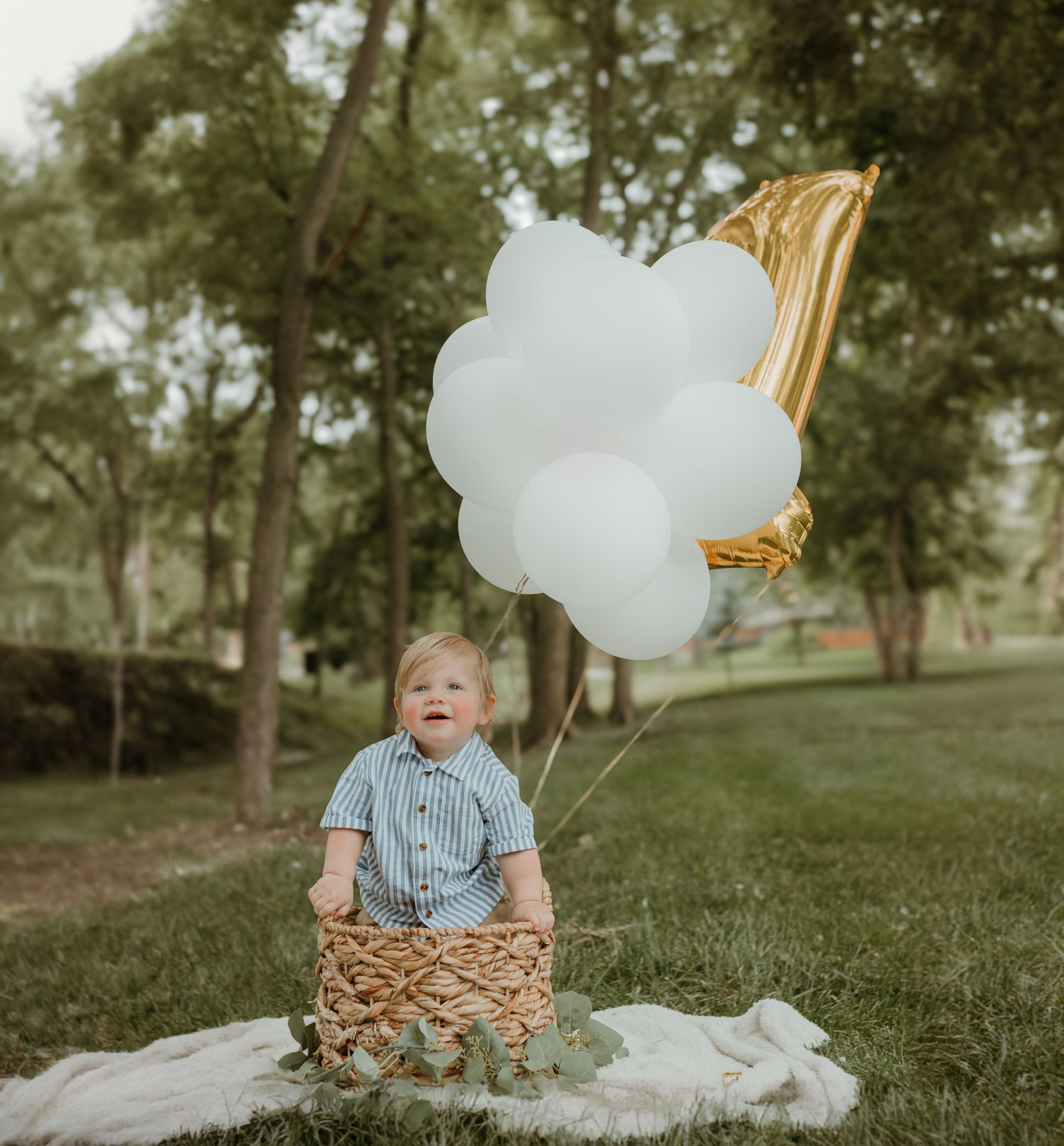 A whimsical outdoor setup with white and gold balloons and a woven basket on a blanket. Colorado Springs Photographer.