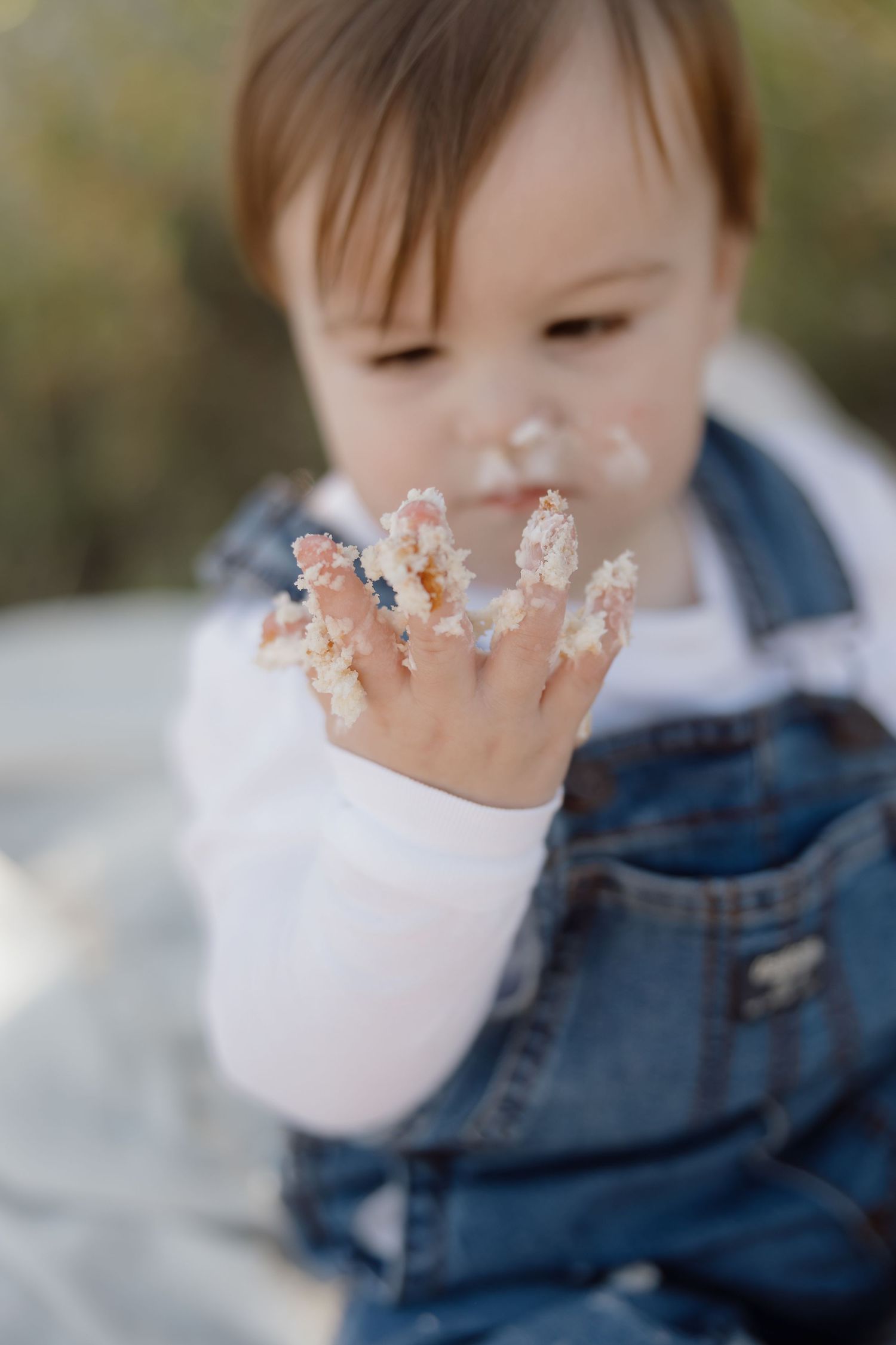 A child wearing a denim jacket plays with snow on their fingertips while wearing a white face mask.