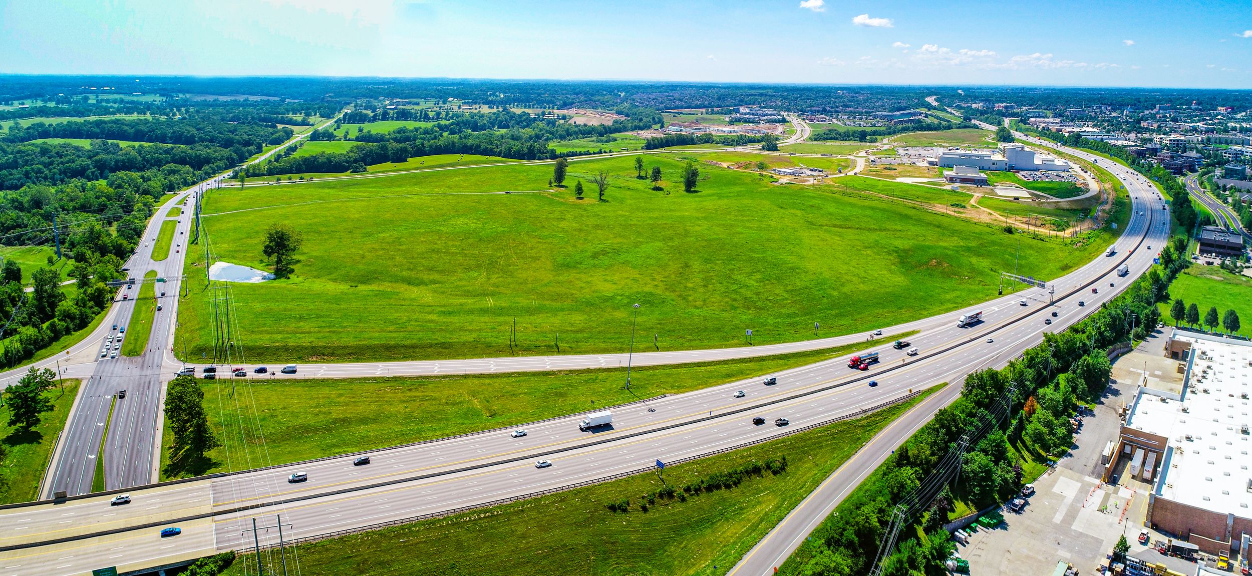 Aerial view of green fields alongside a curved highway interchange with light traffic.