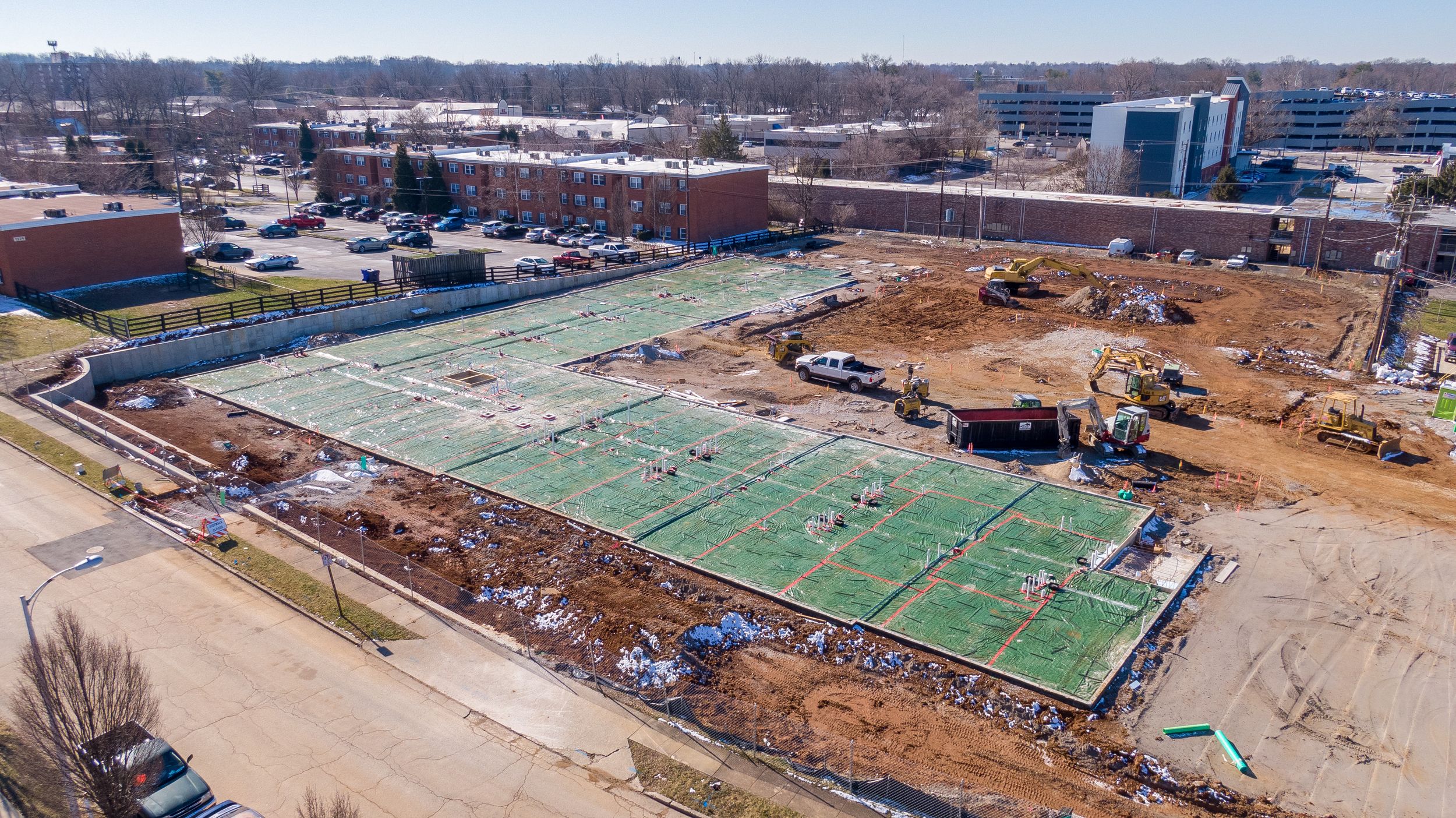 Aerial view of a construction site showing a partially completed sports field with green turf and surrounding earthworks.