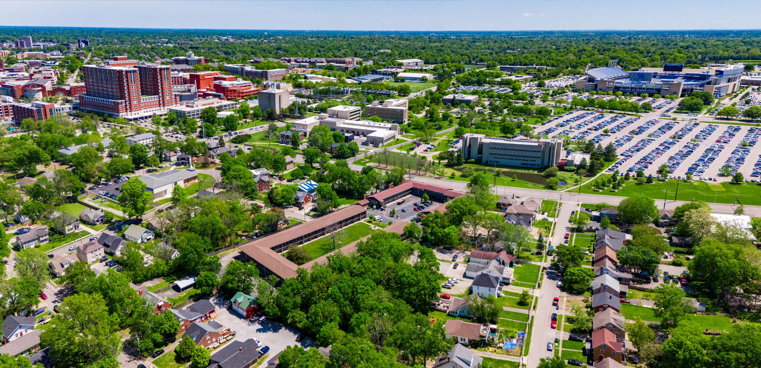 Bird's eye view of an urban area with residential neighborhoods and commercial buildings among green trees.