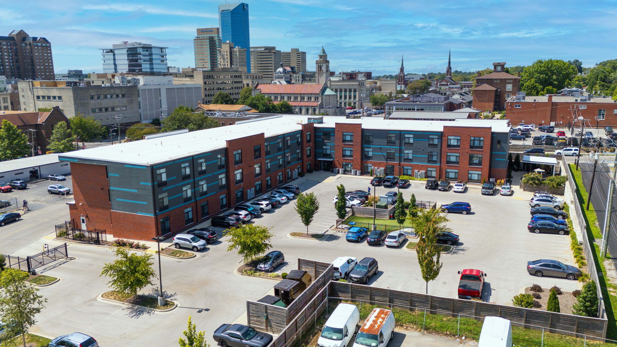 Aerial view of a red brick apartment complex with parking lot in an urban setting.