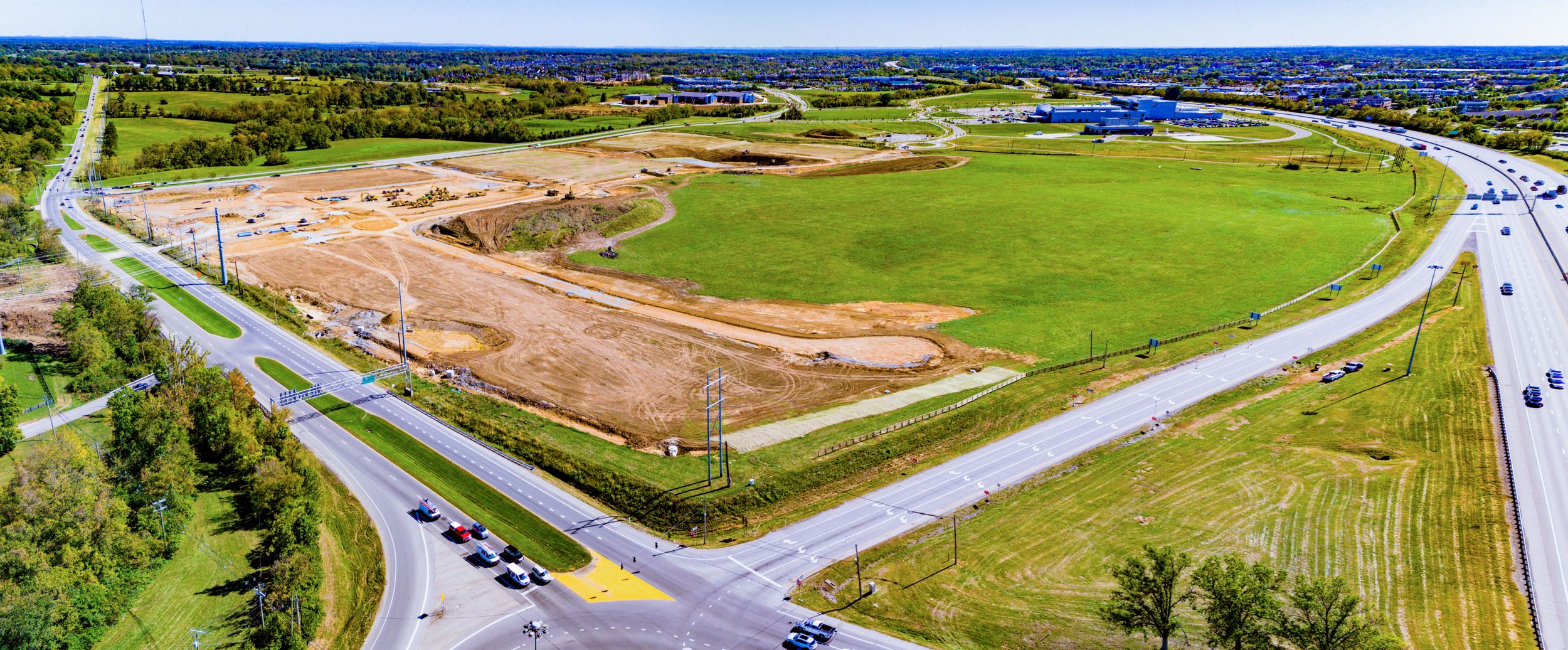Drone shot of an undeveloped land parcel bordered by roads with construction preparation underway.