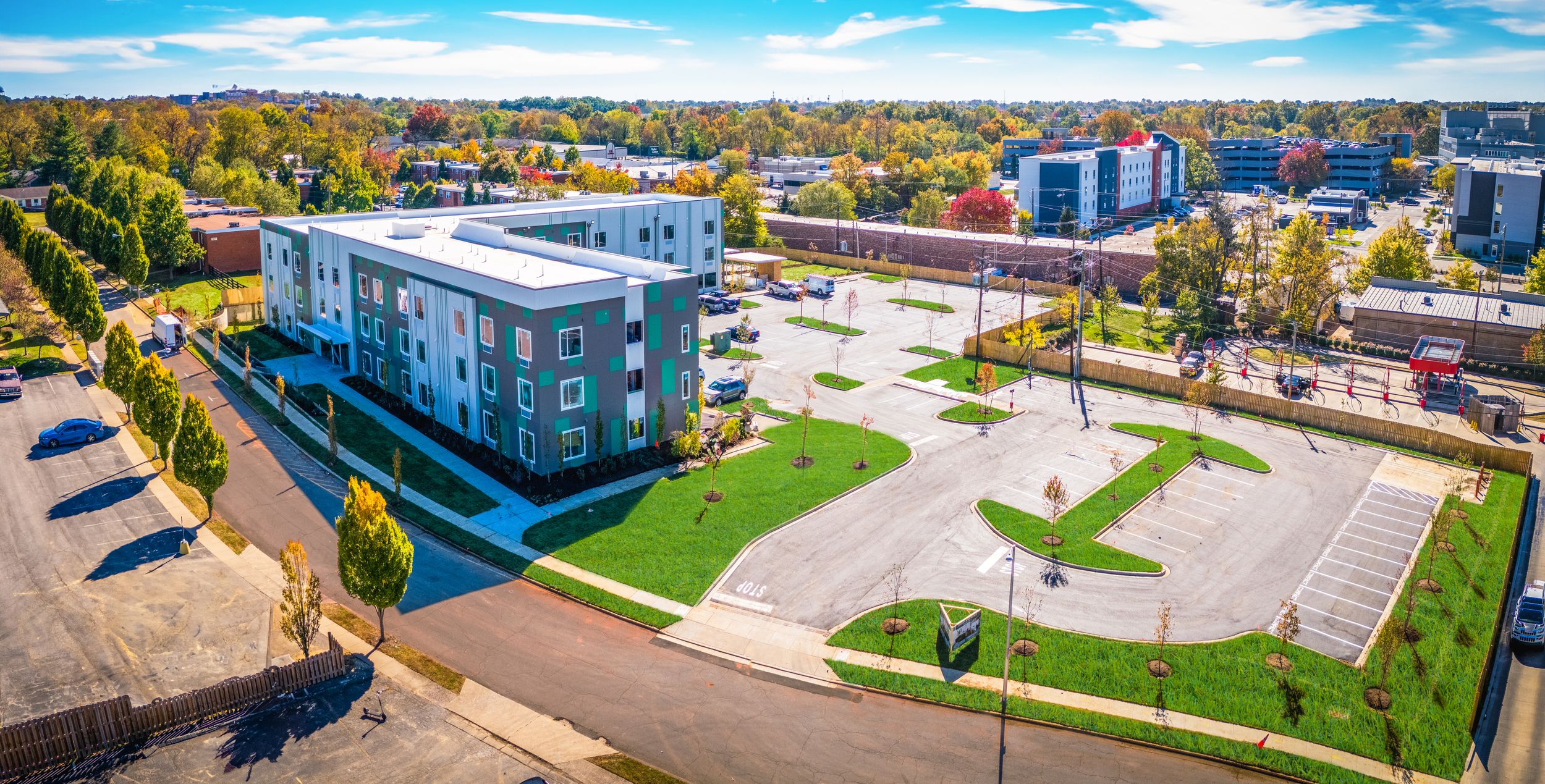 Modern apartment building with white exterior and parking lot viewed from above on a sunny day.