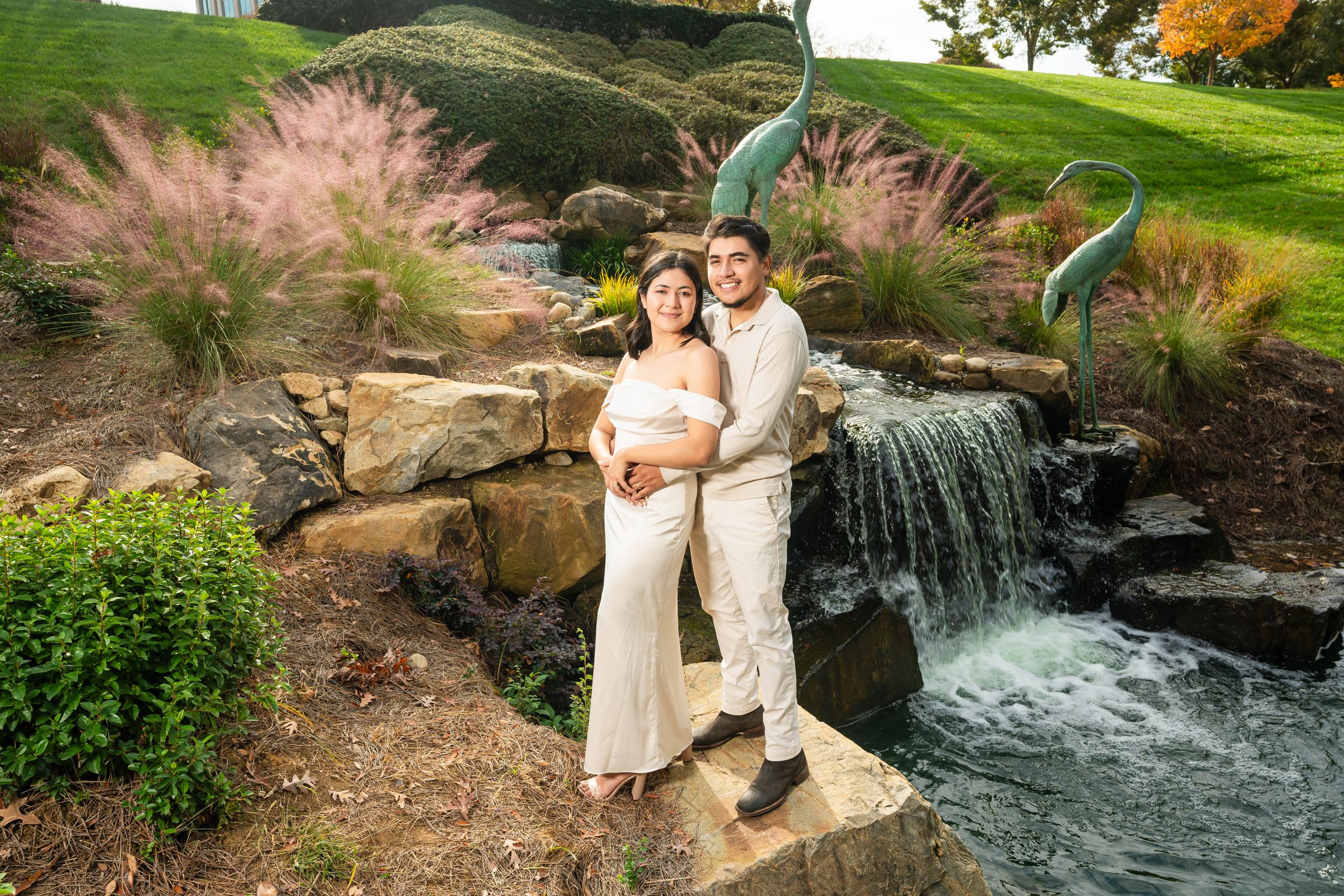 An engagement portrait by a waterfall with ornamental grasses in the background.