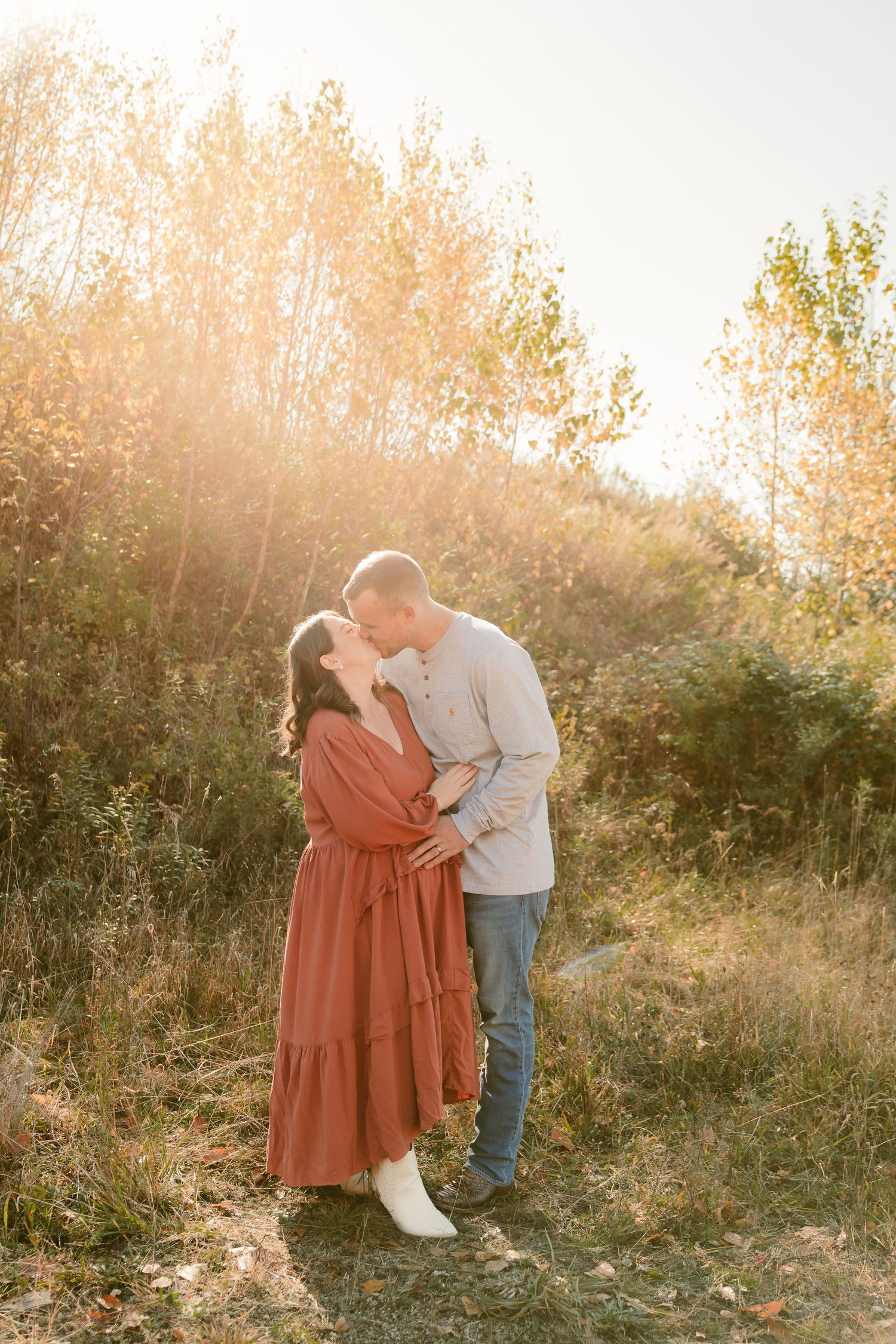 Couple embracing in rustic field during golden hour sunset.