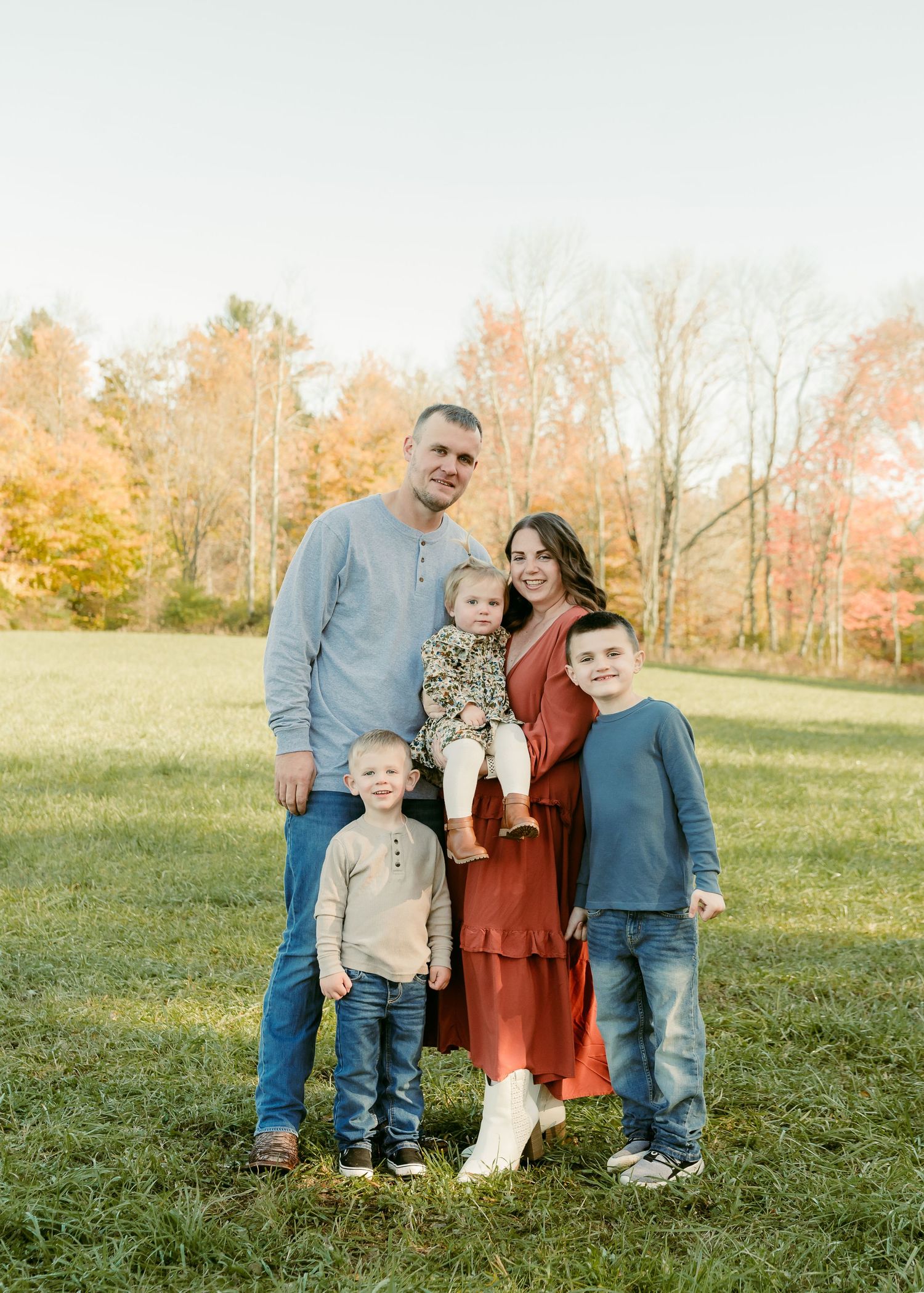 Family of five posing together in autumn field at sunset.