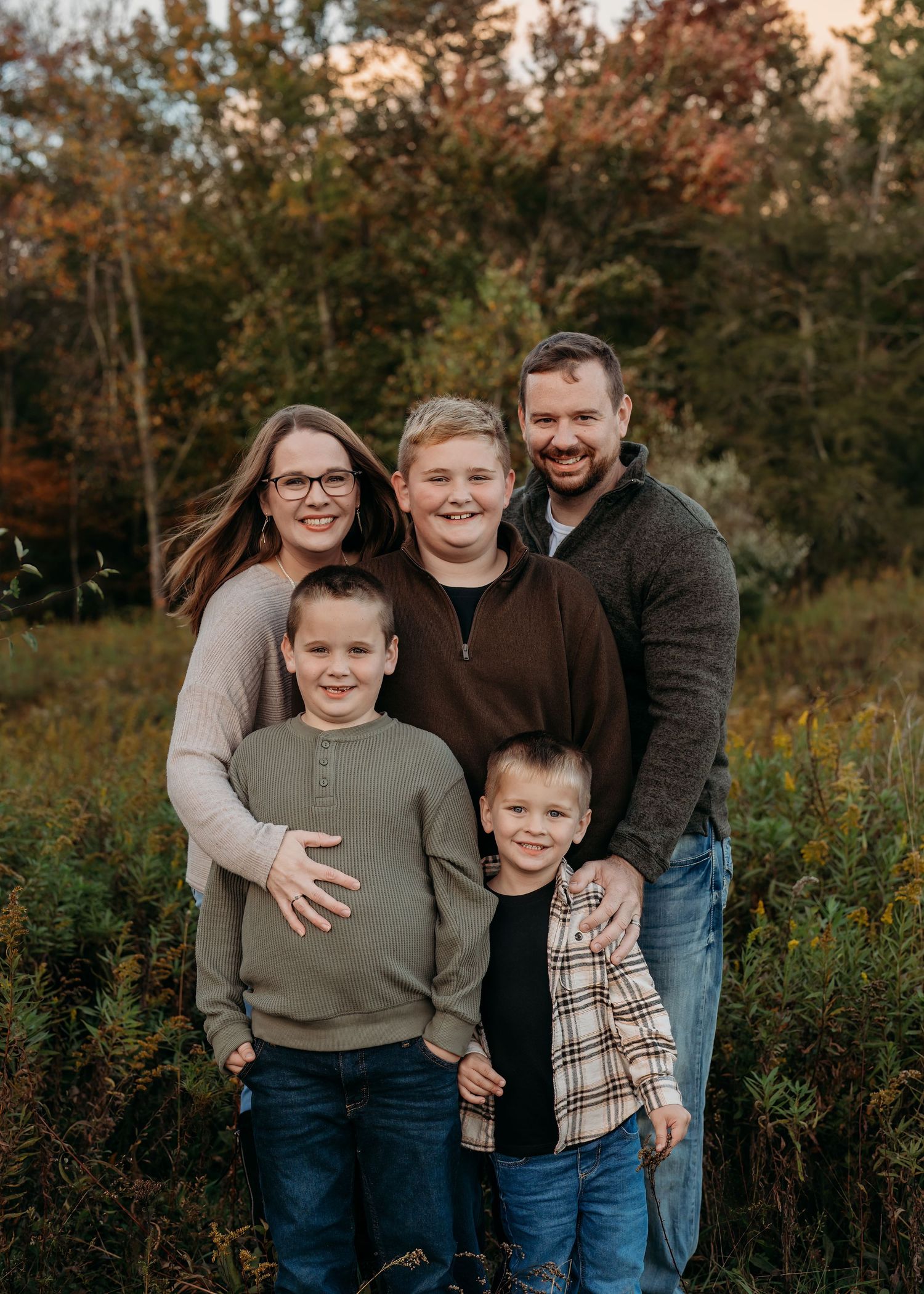 A family of five standing close together outdoors during autumn.