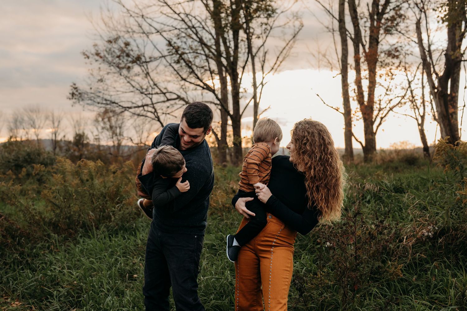 Couple holding children while standing in natural setting during sunset.